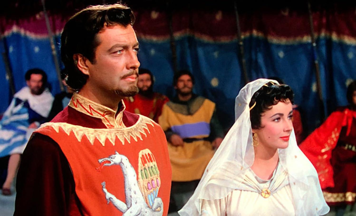 Ein Mann in roter und goldener Kleidung steht neben einer Frau mit weißem Schleier. Im Hintergrund sind Figuren zu sehen, die Szene wirkt historisch.