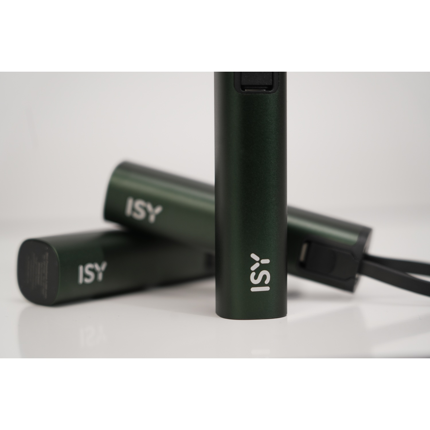 Tre dispositivi cilindrici verde scuro con 'ISY' stampato, disposti su una superficie bianca. Uno è a fuoco.