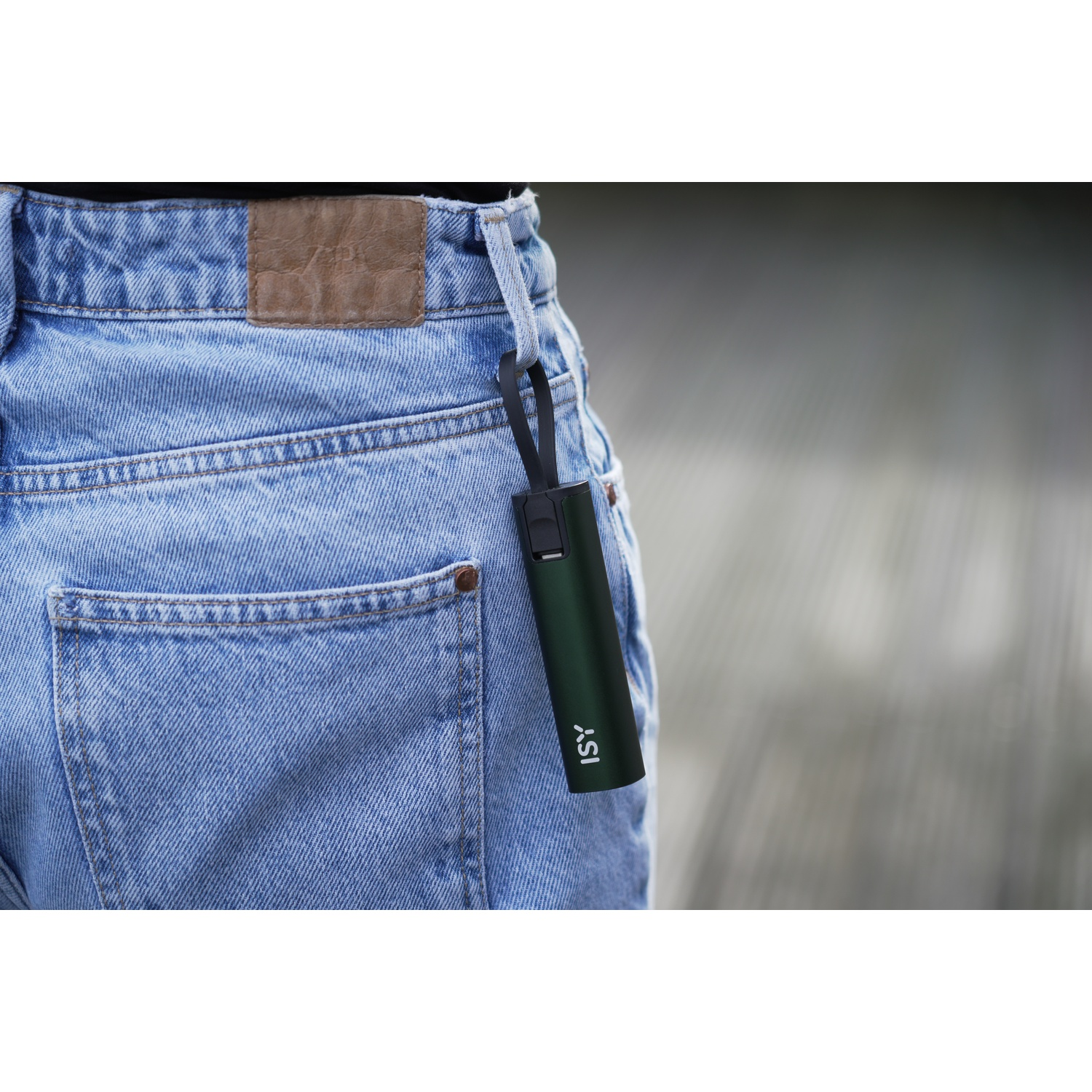Una persona indossa jeans blu. Un dispositivo ISY verde è appeso al passante della cintura. Lo sfondo è sfocato. L'attenzione è sul dispositivo e sui jeans.