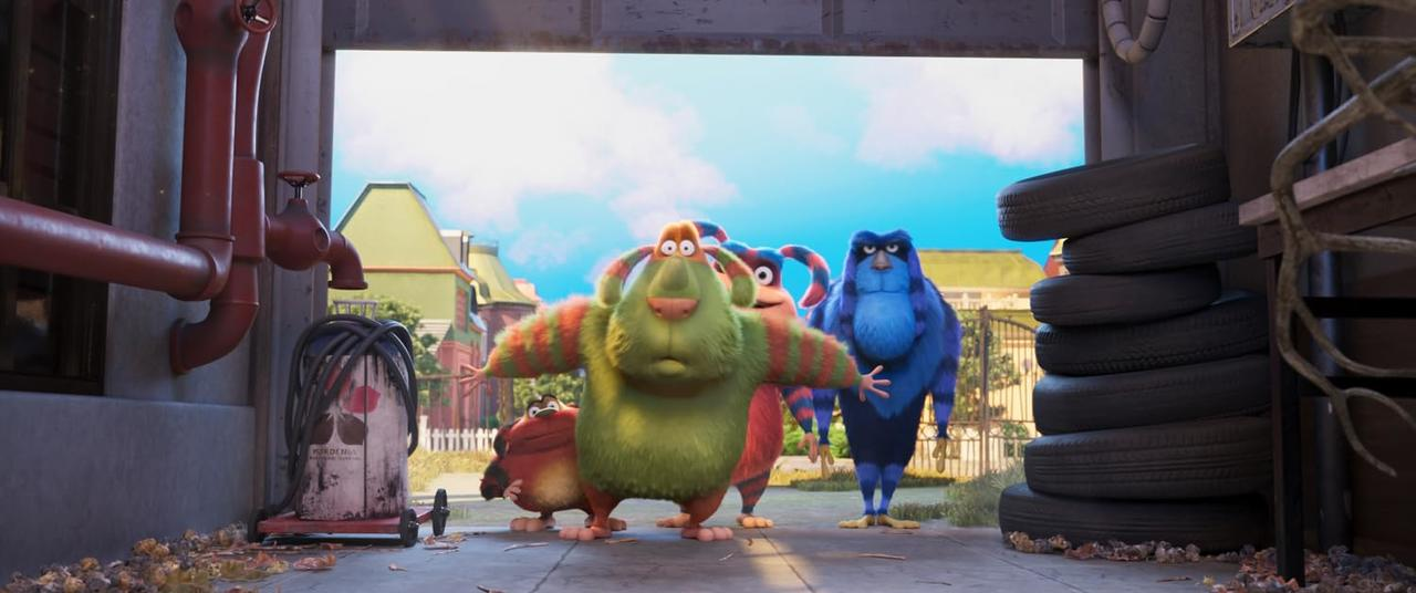 Vier bunte monsterartige Kreaturen stehen vor einer Garage. Blauer Himmel im Hintergrund mit einem Haus. Reifen sind rechts gestapelt.