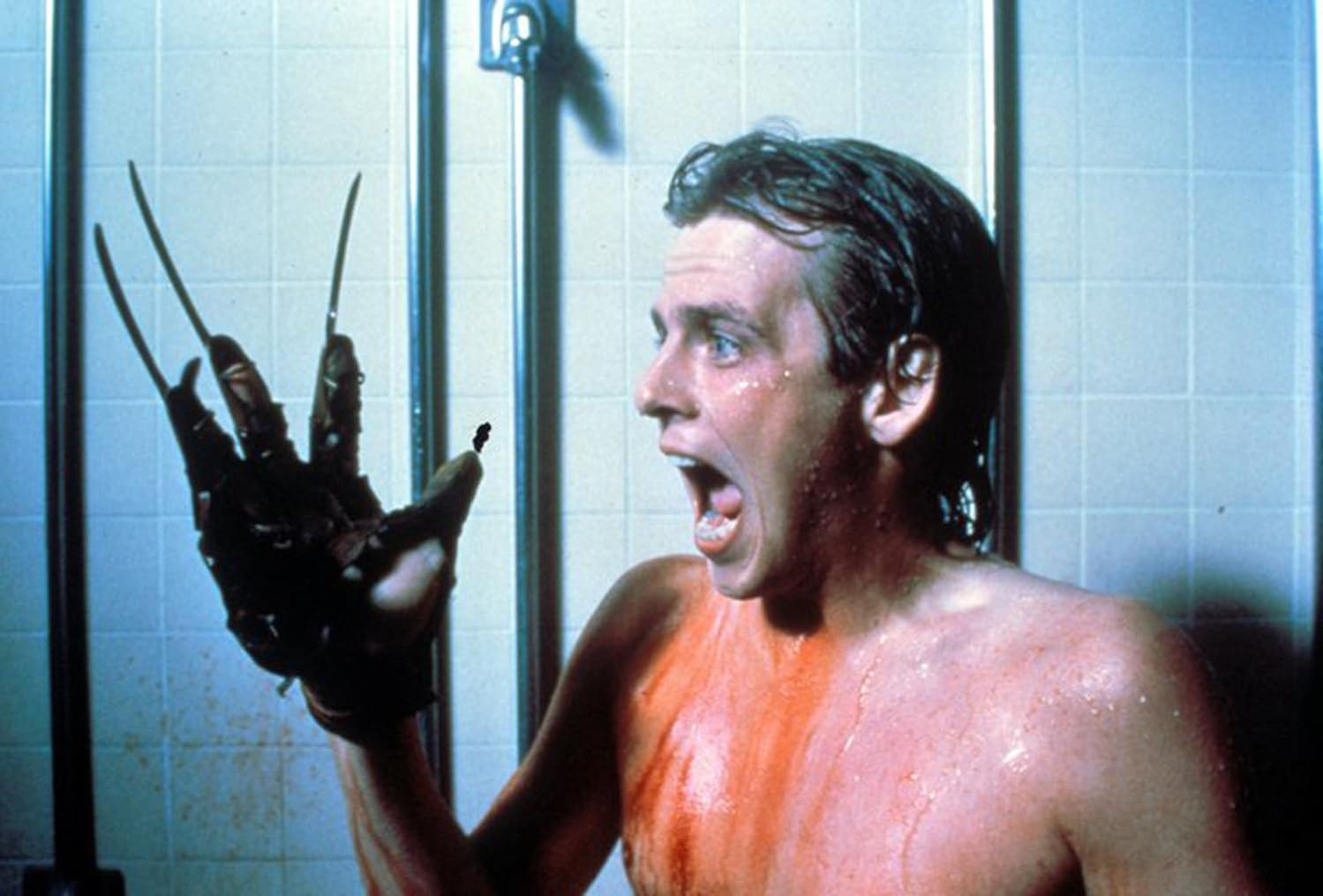 Schreiender Mann, blutbedeckt, mit einer Krallenhand konfrontiert. Szene in einer Dusche, mit blauen Fliesen und Duschkopf im Hintergrund.