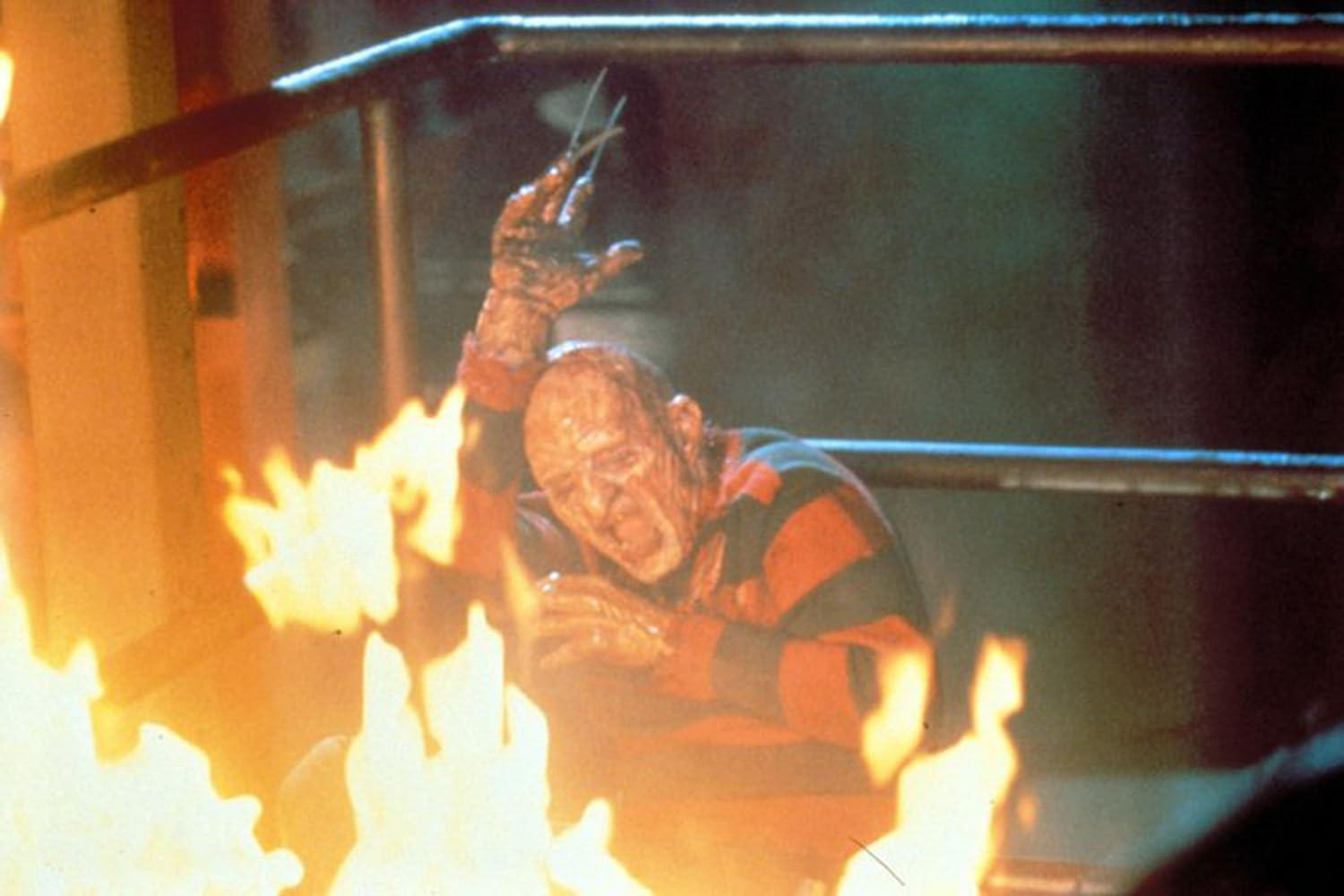 Freddy Krueger in rot-grün gestreiftem Hemd mit Klingenhandschuh, umgeben von Feuer. Der Hintergrund ist eine dunkle Metallkonstruktion.