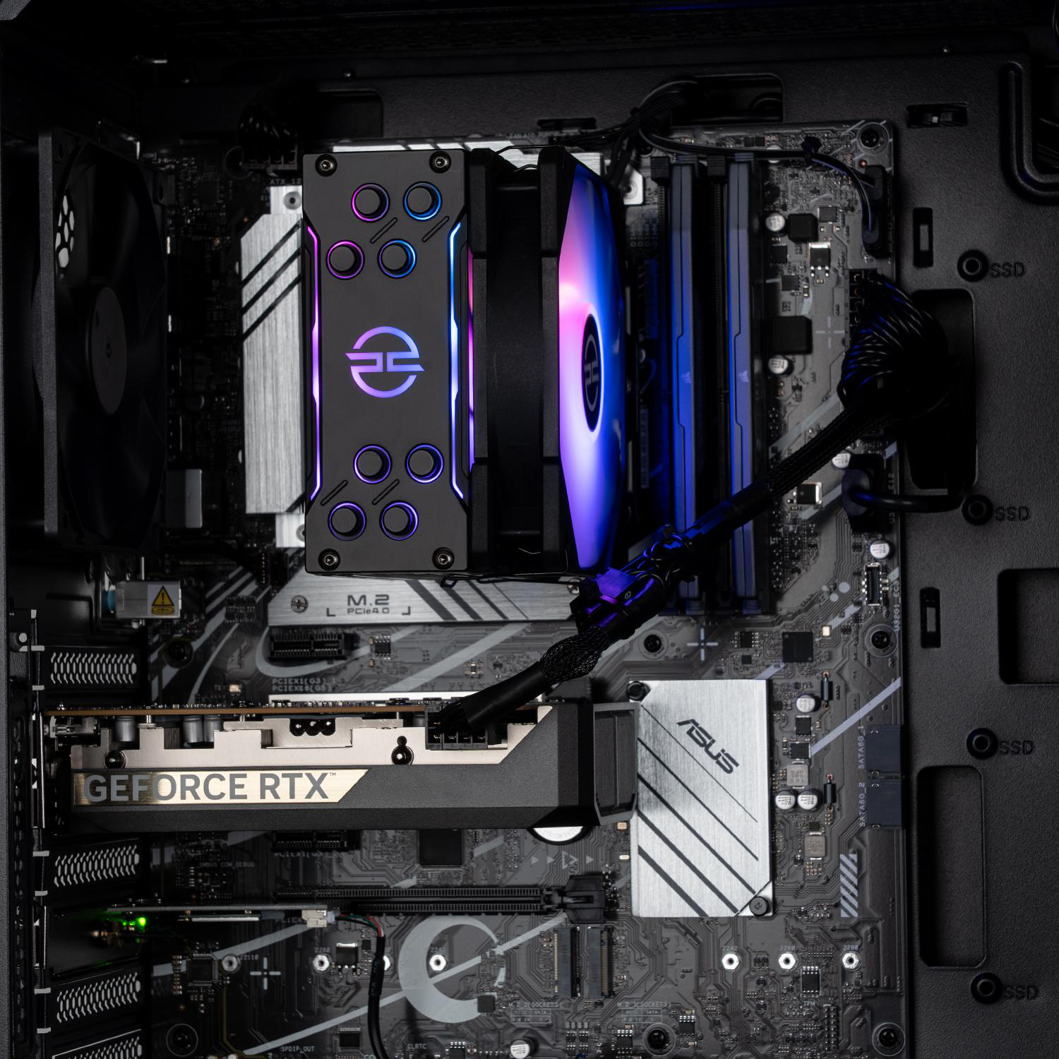 In einem Computergehäuse sind Komponenten sichtbar: ein CPU-Kühler mit RGB-Beleuchtung, eine Grafikkarte, ein Motherboard mit ASUS-Logo.