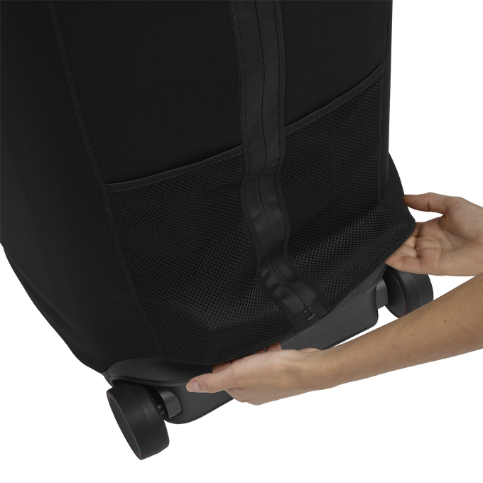 Hände halten eine schwarze Kofferhülle. Der Koffer hat eine Netztasche und Räder. Die Hülle wird über den Koffer gezogen.