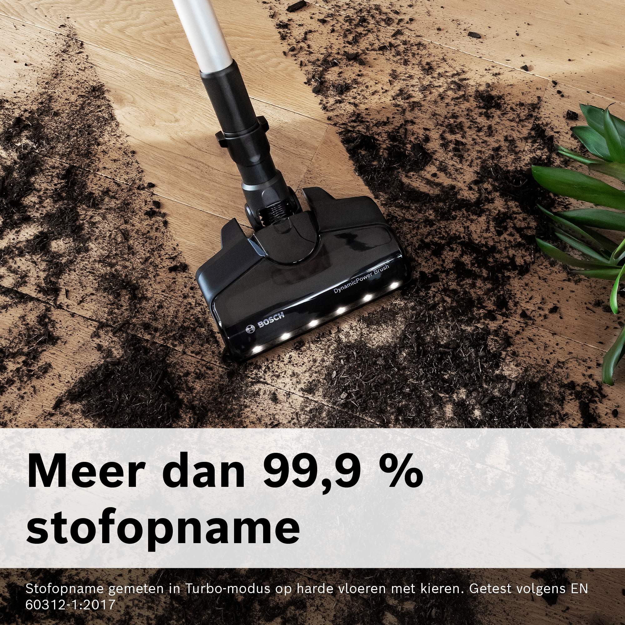 A black vacuum cleaner head on a wooden floor covered in dirt. A plant is to the right. Text says 99.9% dust capture.