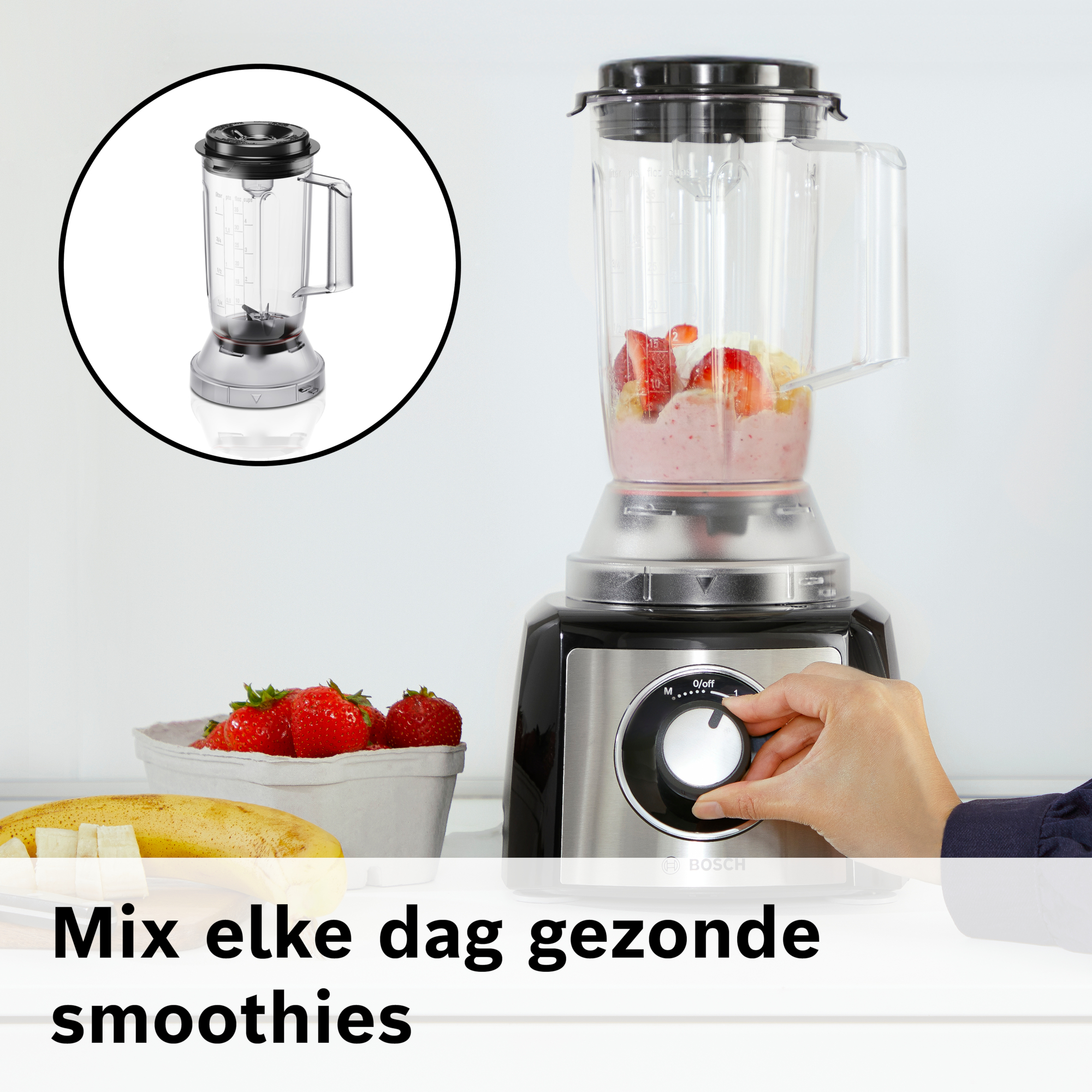 Een blender met fruit erin, aardbeien en bananen op tafel, en een hand die aan de knop draait.