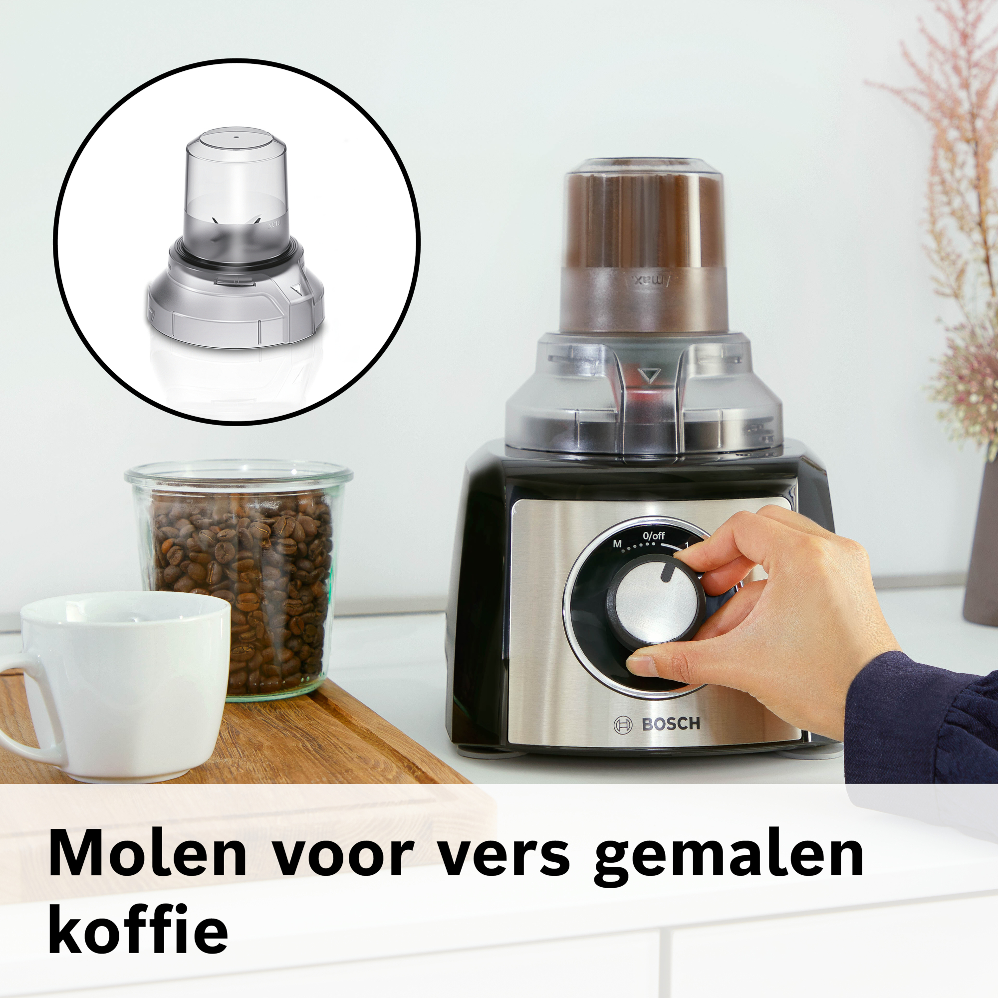 Koffiemolen. Een hand draait aan de knop van een Bosch-apparaat. Pot bonen en een kopje staan op een houten dienblad.