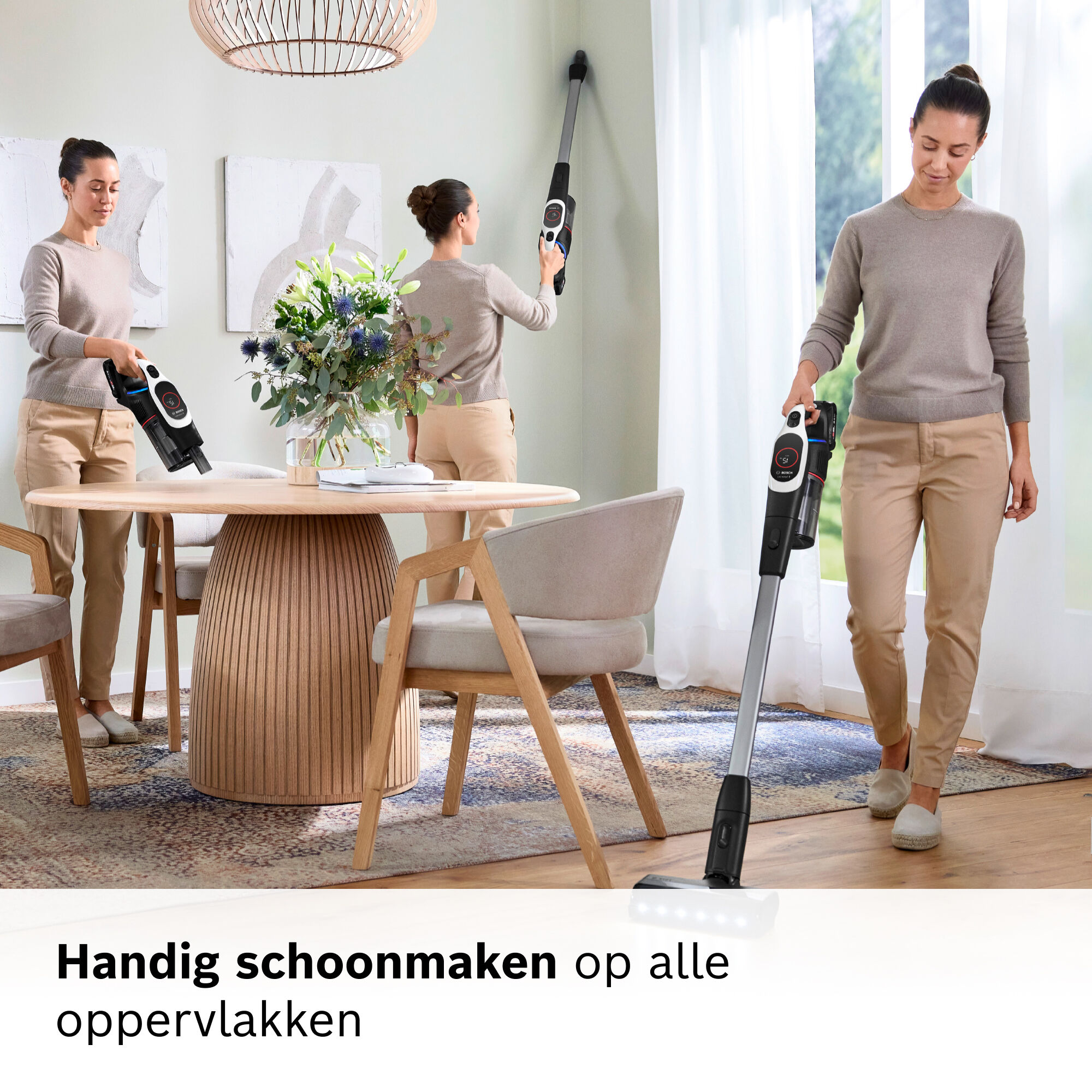 Woman vacuums a room. She is using a cordless vacuum cleaner. Background shows a table, chairs, flowers, and window.