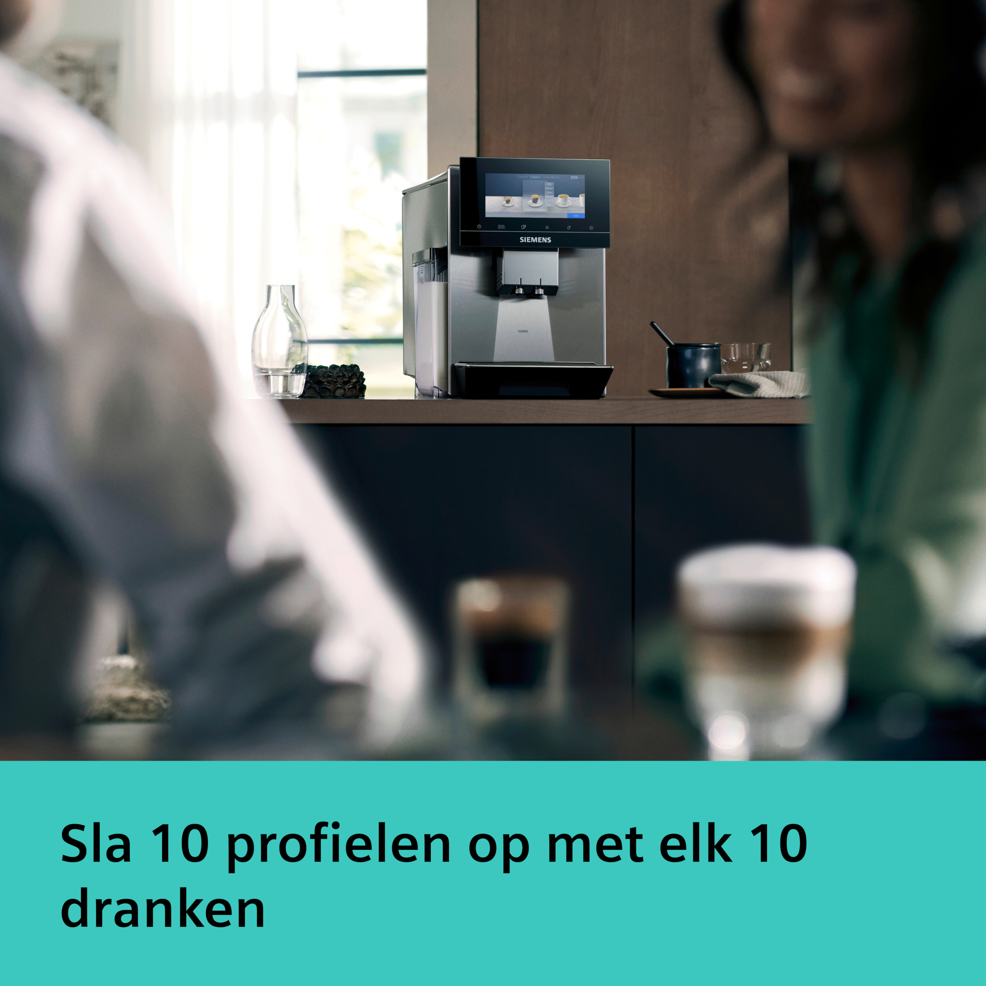 Coffee machine with touch screen. In front, two blurred people. Two coffee glasses in the foreground.