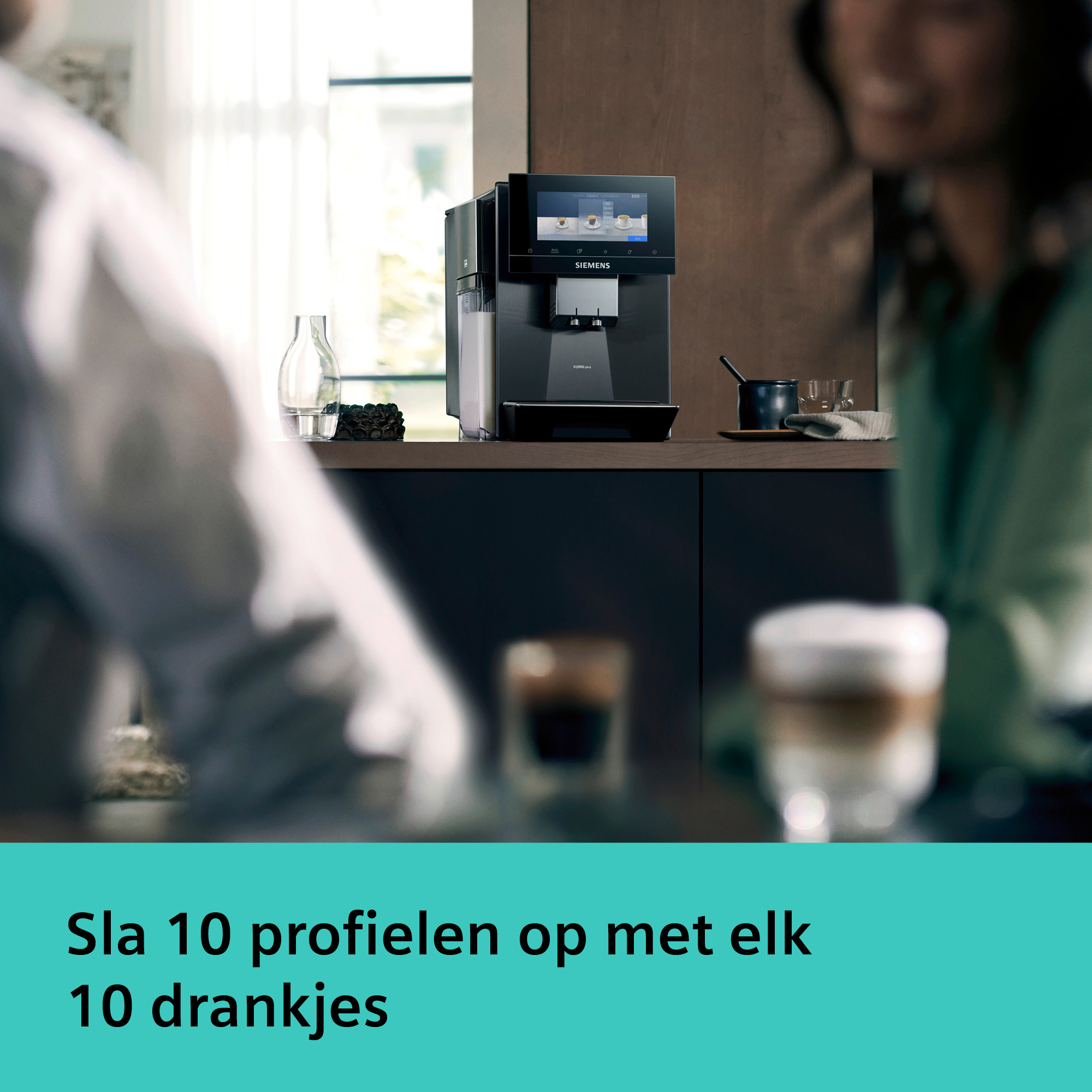 A coffee machine on a counter, with two blurry people in the foreground and a glass of coffee.