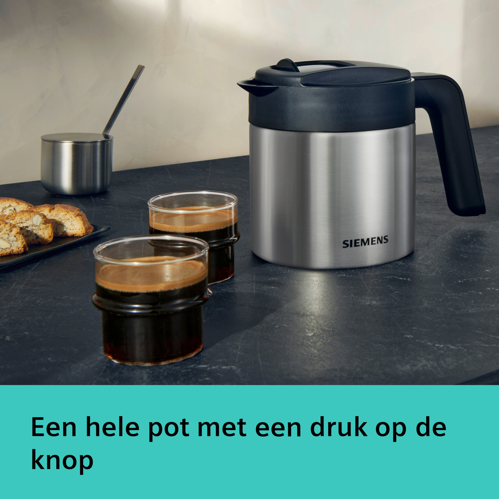 A stainless steel coffee pot and two glasses of coffee sit next to a tray of cookies on a dark surface.