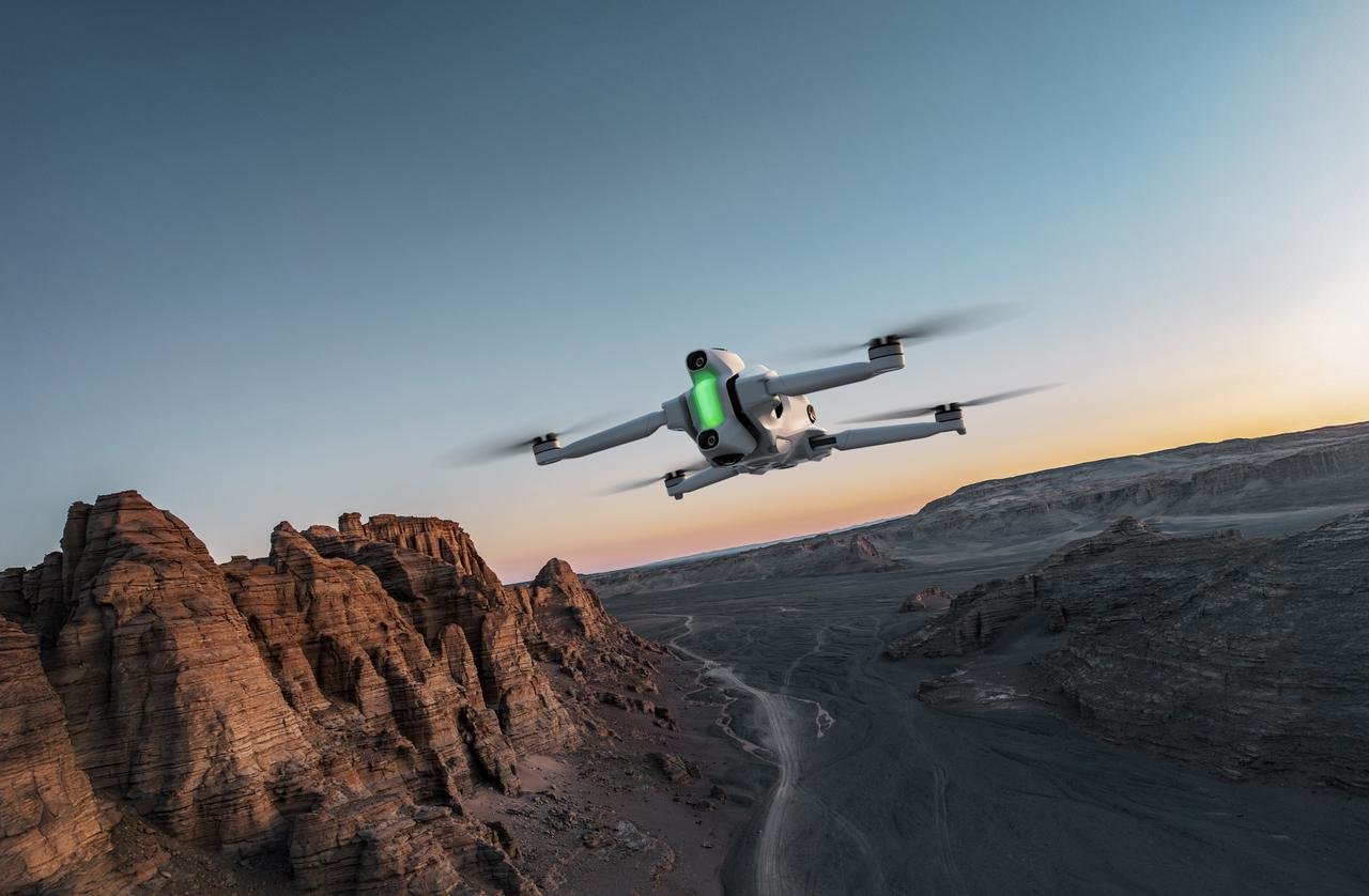 Un drone bianco vola sopra un paesaggio del canyon al tramonto. Il cielo è blu e arancione. Il drone ha luci verdi.