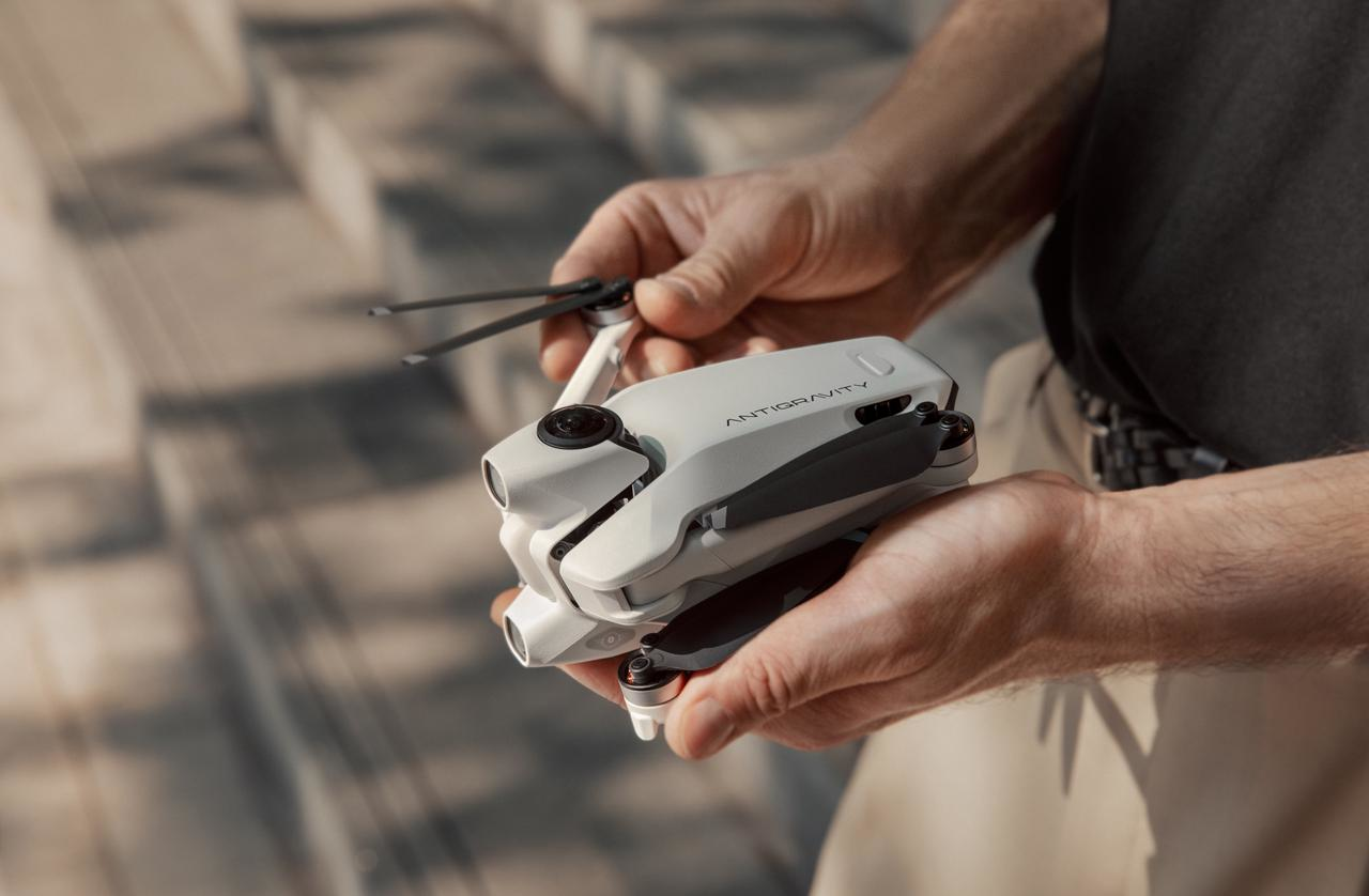 Una persona tiene in mano un drone bianco e grigio. Il drone ha la scritta ANTIGRAVITY. Lo sfondo è sfocato.