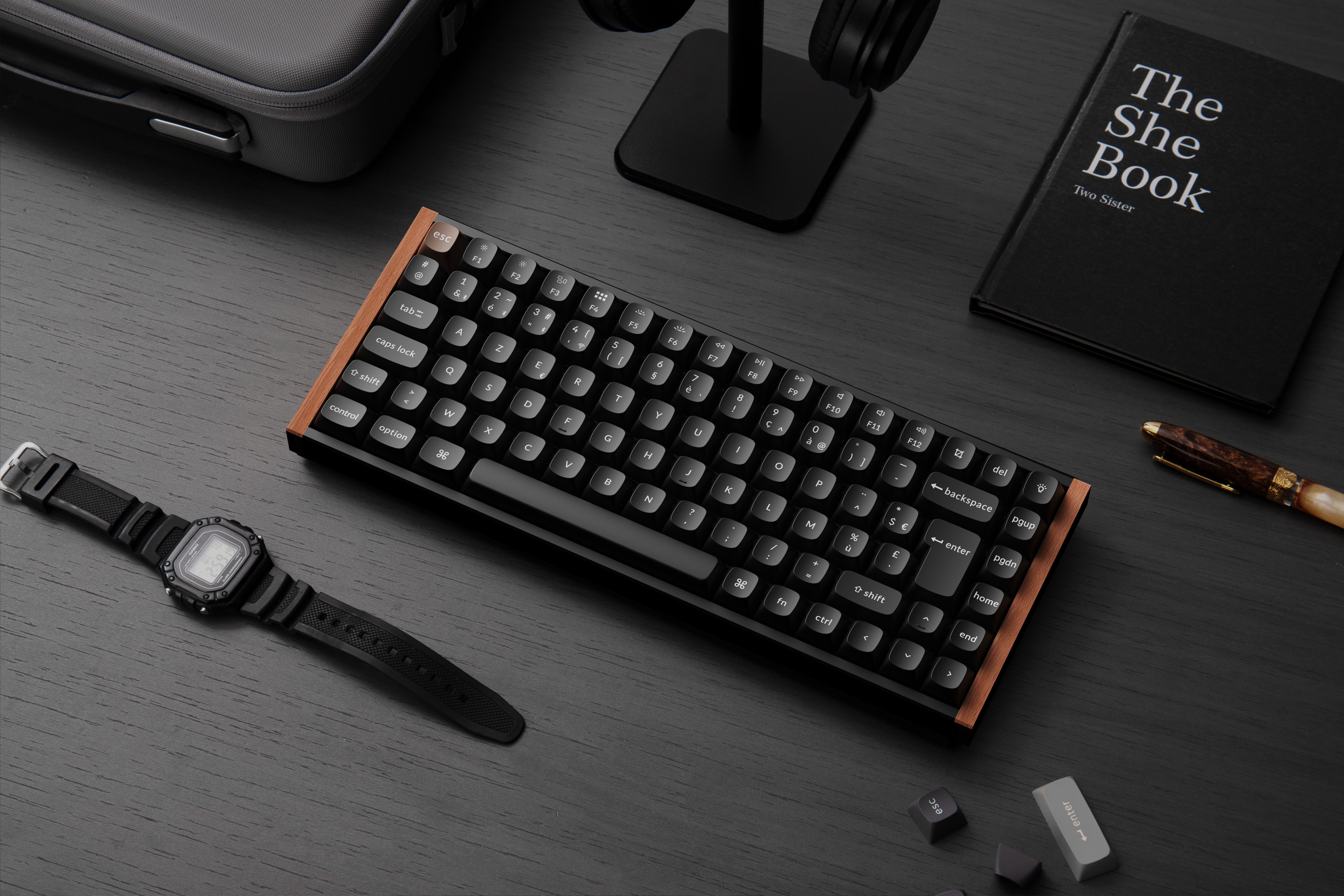 Schwarze Tastatur mit Holzrahmen und Uhr auf einem schwarzen Schreibtisch. Buch und Kopfhörer sind ebenfalls vorhanden.