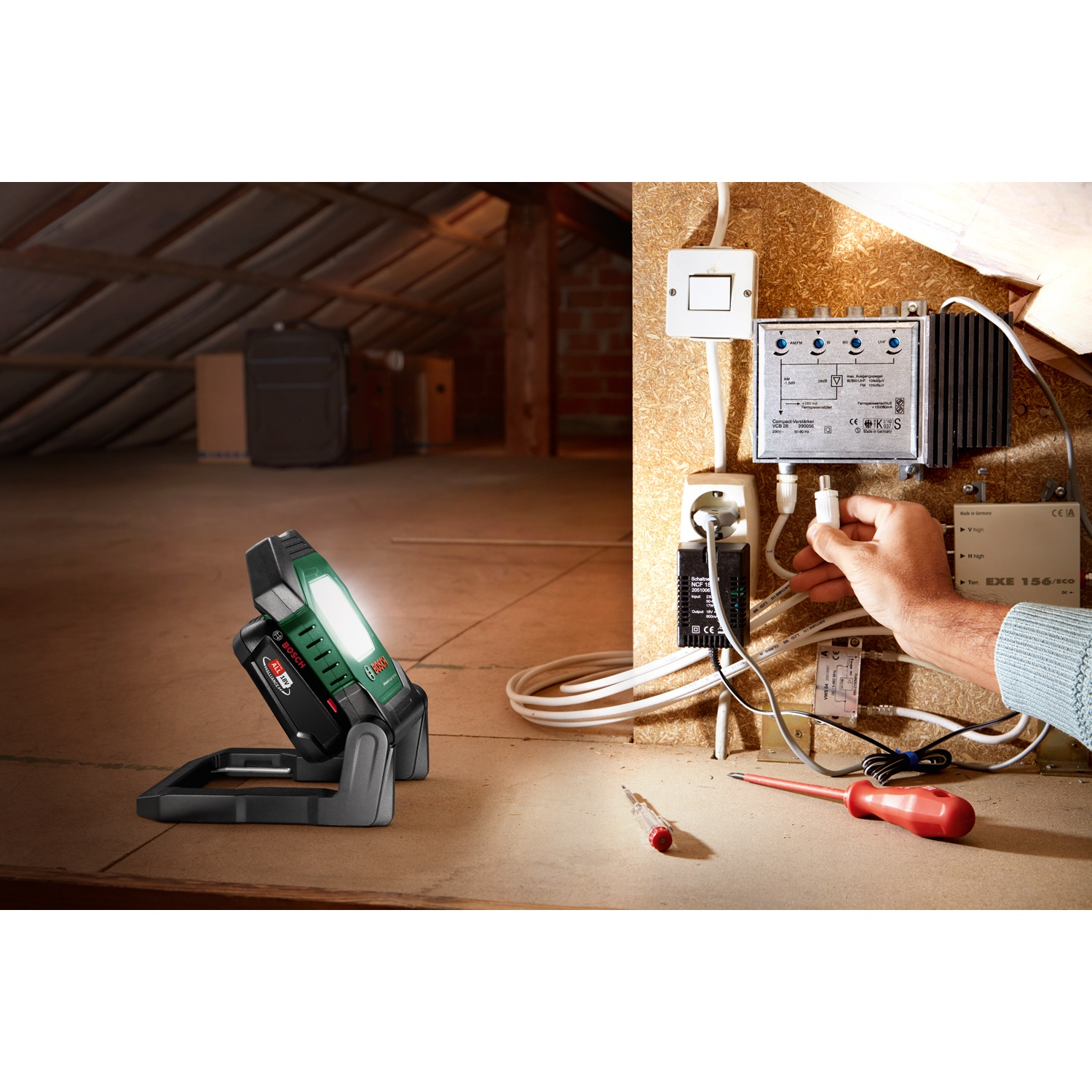Una lampada da lavoro Bosch illuminata è su una superficie di legno. Una persona collega un cavo vicino a componenti elettrici.
