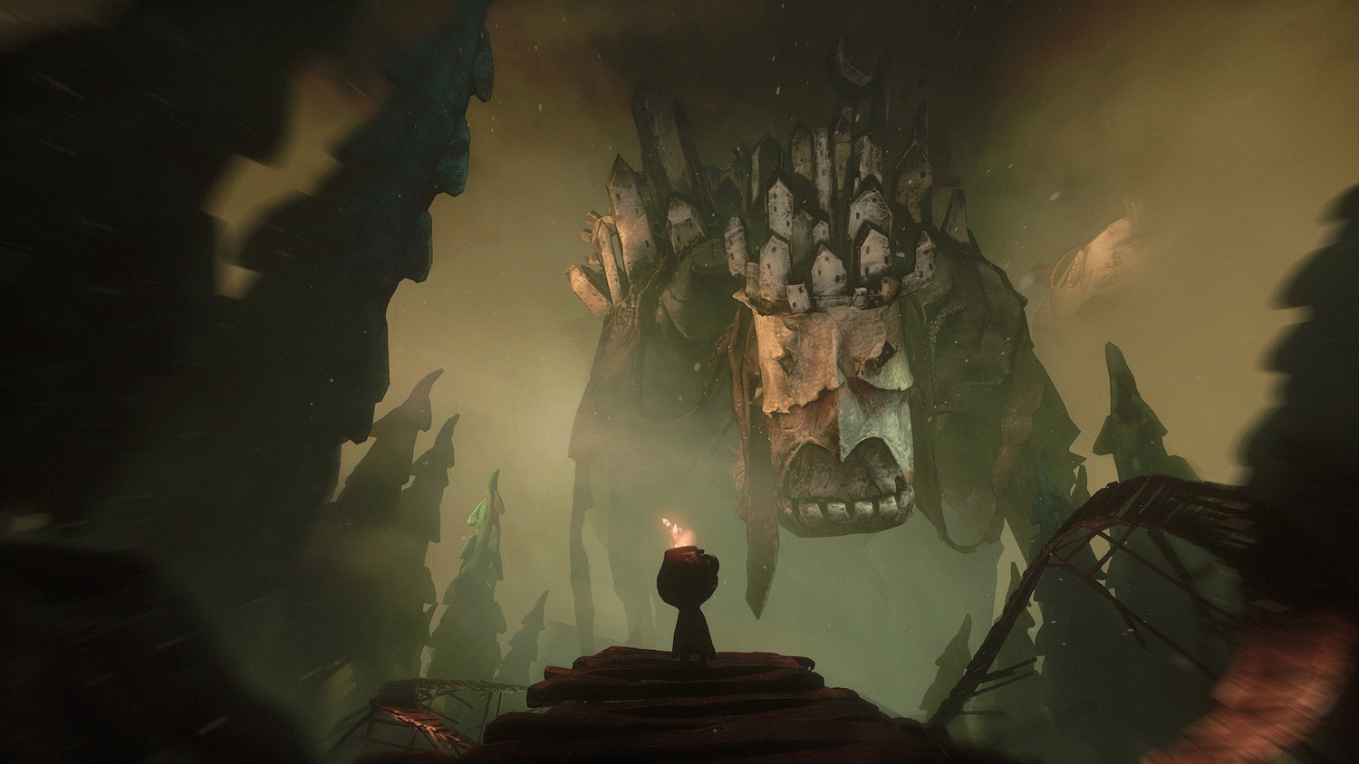 Una pequeña figura se para frente a una estructura esquelética gigante. La escena es brumosa con una antorcha en la figura.