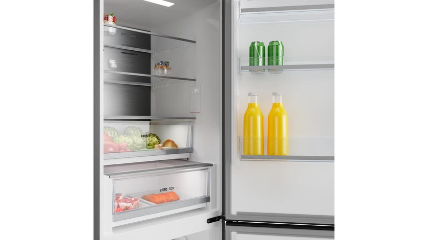Refrigerador abierto lleno de productos, jugo y bebidas enlatadas. Verduras y carne en cajones. Botellas de jugo amarillo visibles.