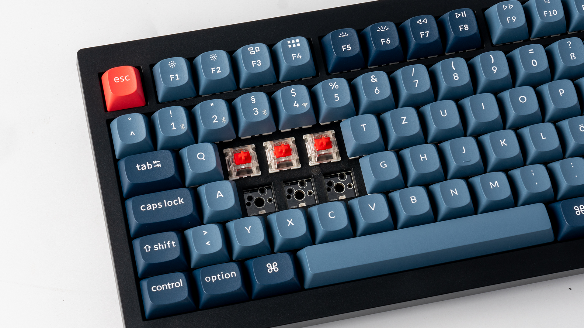 Nahaufnahme einer mechanischen Tastatur mit blauen Tasten, einer roten Escape-Taste und freiliegenden roten Schaltern.