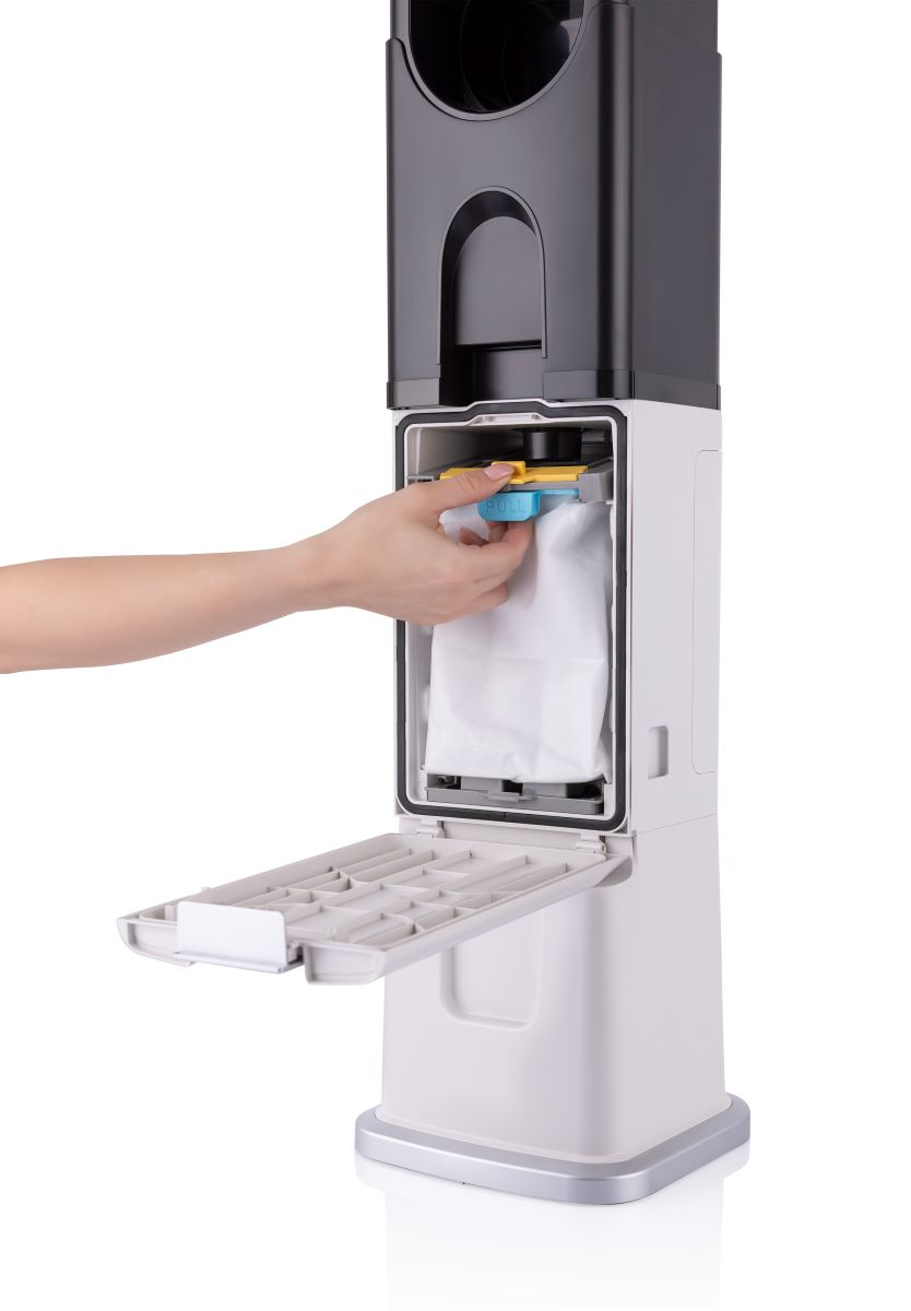 Bir el, beyaz ve siyah bir elektrik süpürgesinden beyaz bir poşet çekiyor. Tepsi açık.