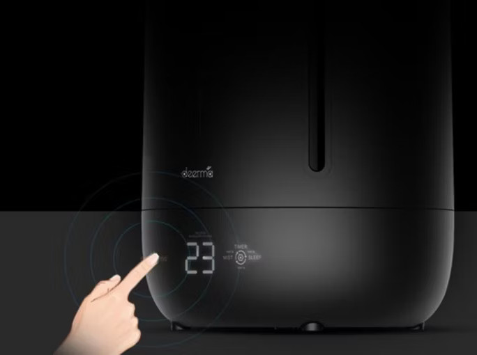 Czarny nawilżacz z cyfrowym wyświetlaczem pokazującym 23. Palec dotyka ekranu. Marka jest widoczna.