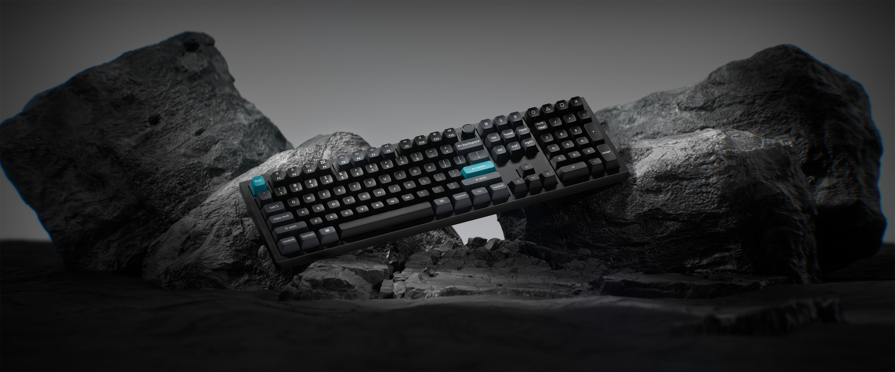 Eine schwarze Tastatur liegt auf dunkelgrauen Felsen. Die Tastenkappen sind schwarz, einige Tasten teal. Der Hintergrund ist ein Farbverlauf.