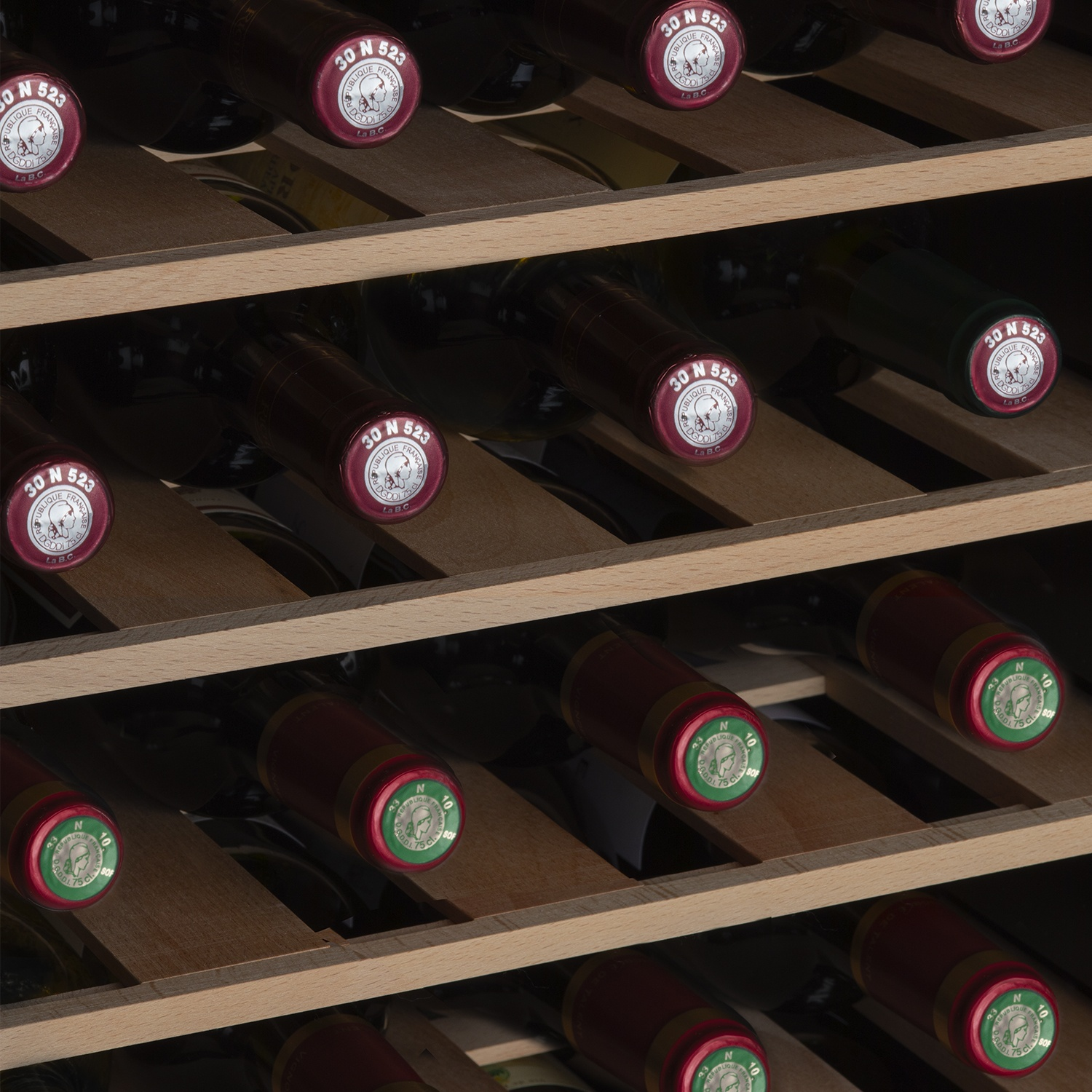 Bottiglie di vino in una rastrelliera di legno. La maggior parte ha tappi rossi con etichette bianche. La rastrelliera è a doghe.