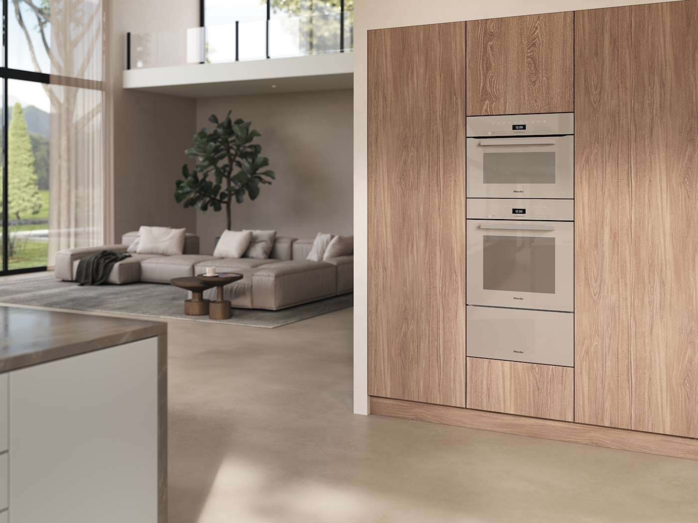 Modernes Kücheninterieur. Zwei Öfen sind in Holzschränke eingebaut. Im Hintergrund ist ein Wohnzimmer mit Sofa zu sehen.