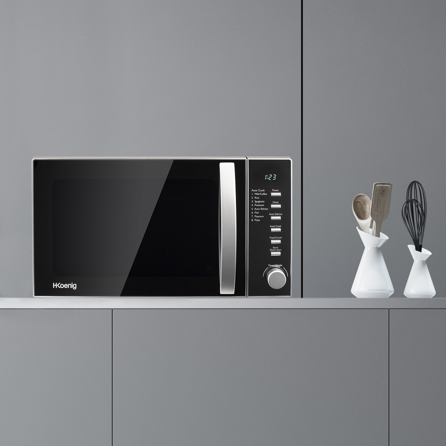 Un forno a microonde con frontalino nero è su una mensola. A destra ci sono vasi bianchi con utensili. Lo sfondo è grigio.