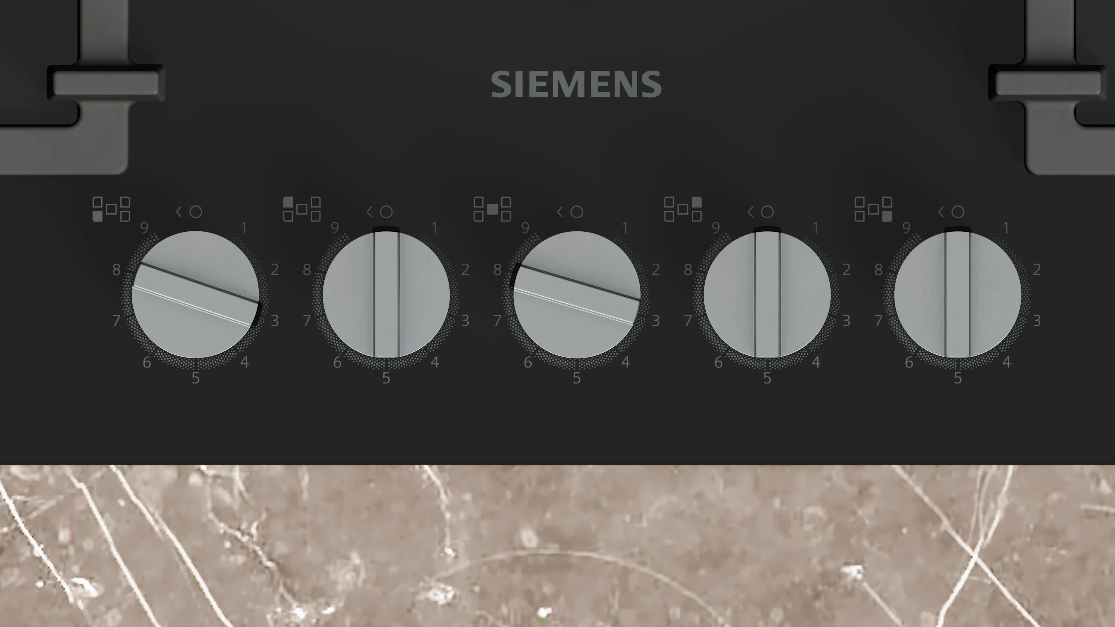 Una encimera negra con cinco perillas plateadas. La palabra SIEMENS está encima de las perillas. La parte inferior es un patrón de mármol marrón.
