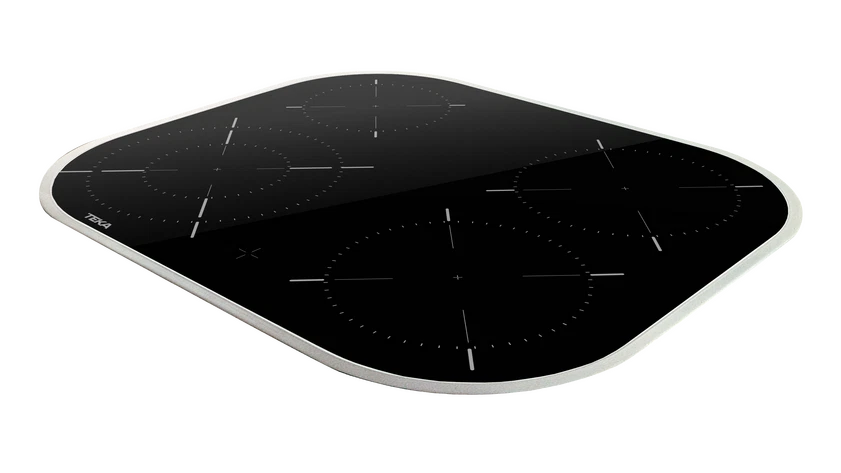 Encimera de inducción de vidrio negro con cuatro zonas de cocción. Tiene un marco plateado y el logo de Teka.