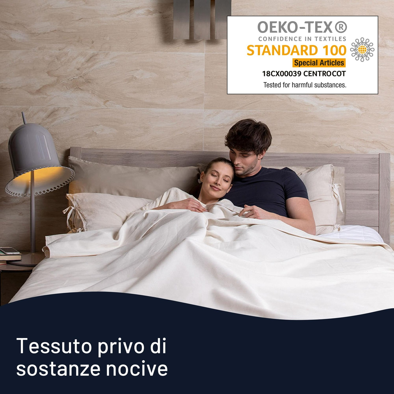 Una coppia è a letto, coperta da una coperta bianca. A sinistra c'è una lampada. Lo sfondo è un muro chiaro e decorato.