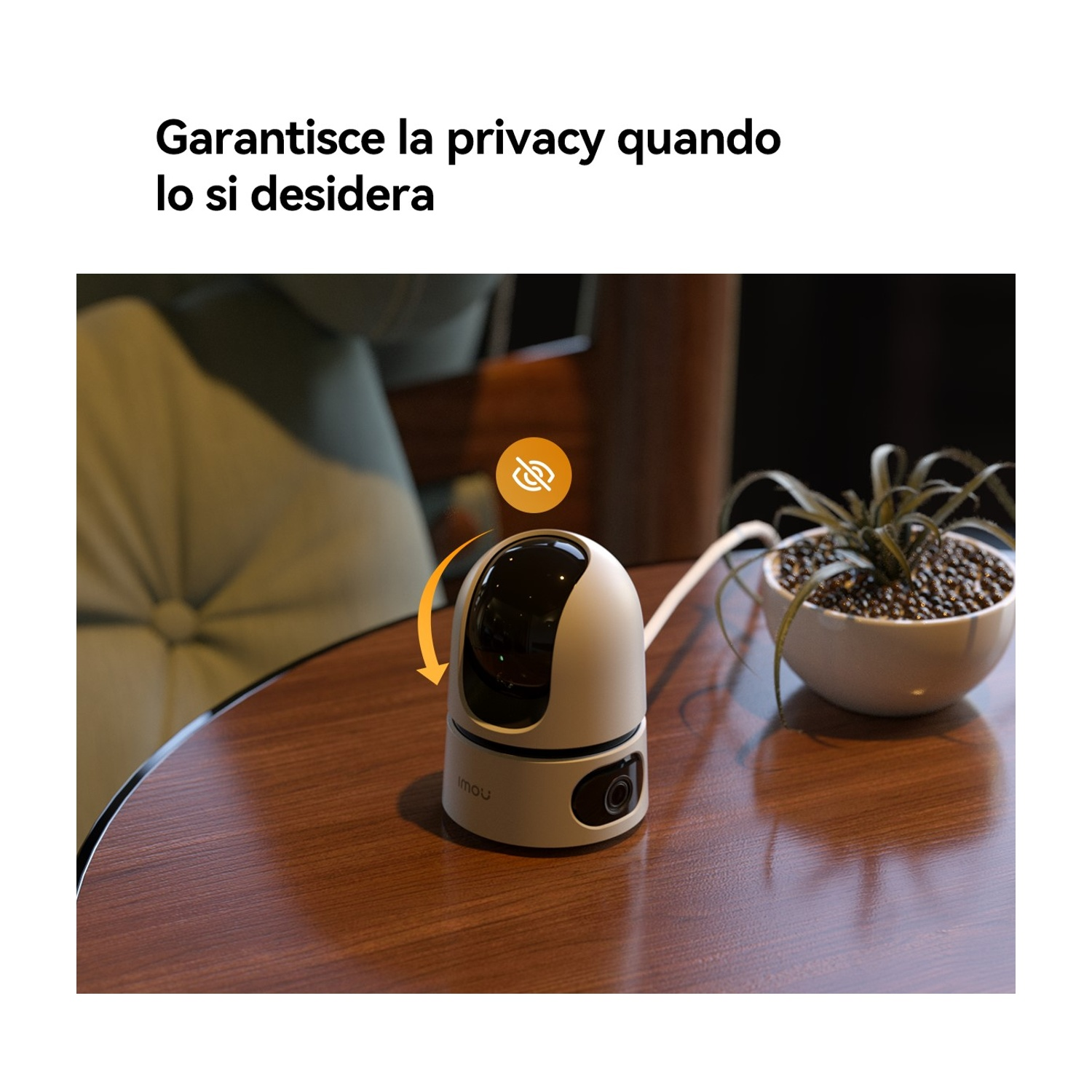 Una telecamera di sicurezza bianca e nera su un tavolo di legno. Accanto c'è una pianta in un vaso bianco. La telecamera ha una freccia arancione.