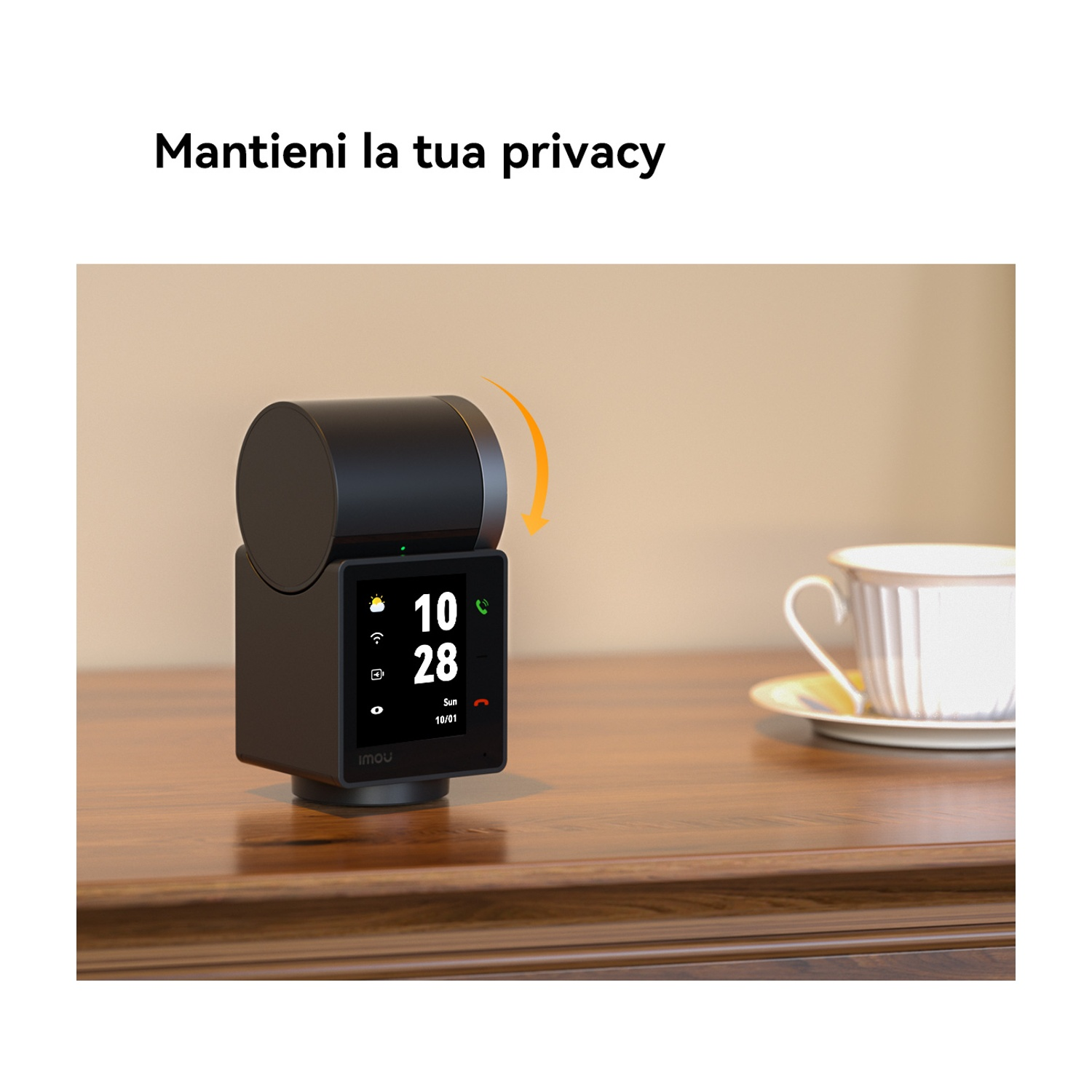 Un dispositivo nero con schermo che mostra l'ora è posizionato su un tavolo di legno. Sullo sfondo una tazza da tè e un piattino.