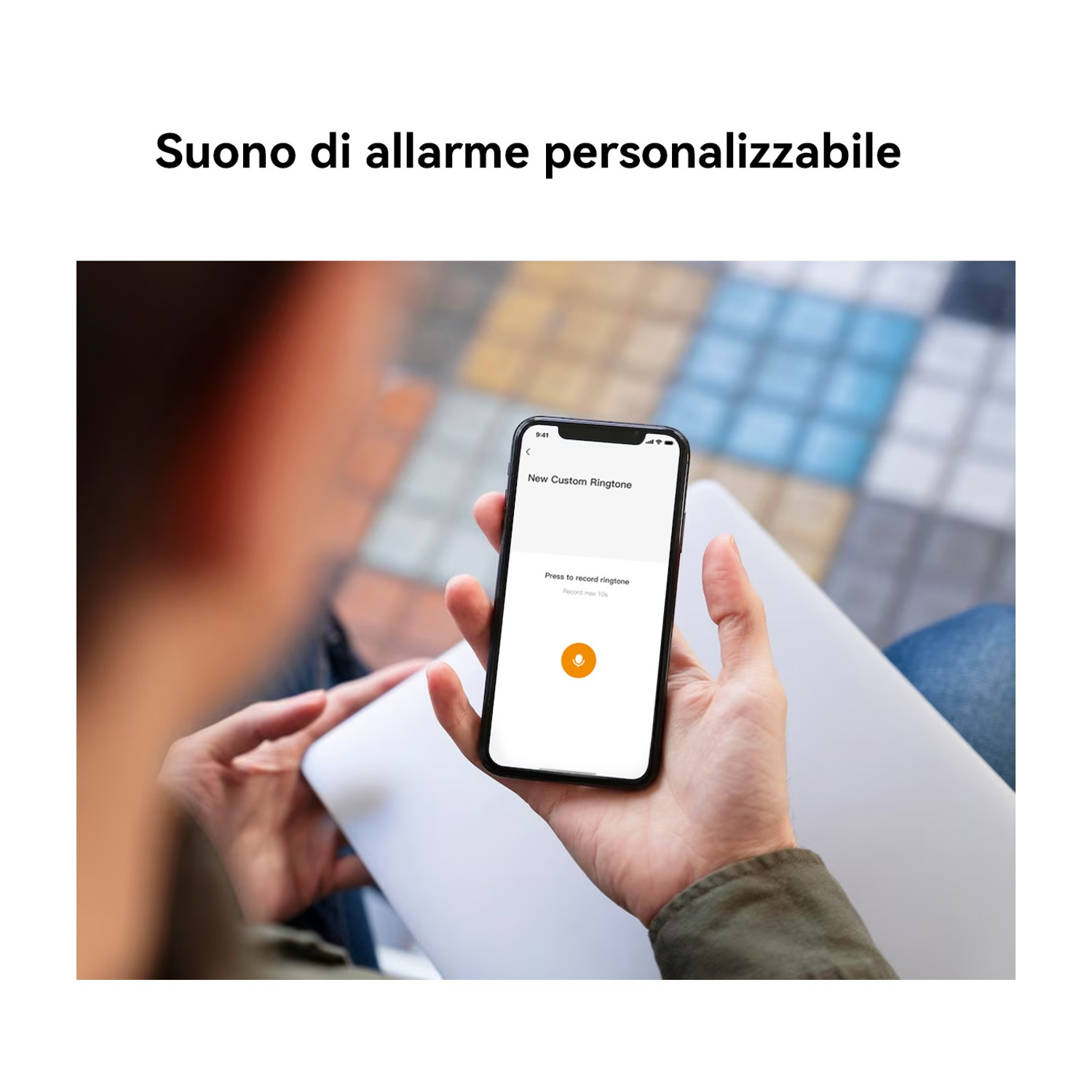 Una persona tiene in mano un telefono con una schermata di suoneria personalizzata. Il telefono mostra un pulsante di registrazione. Lo sfondo è sfocato.
