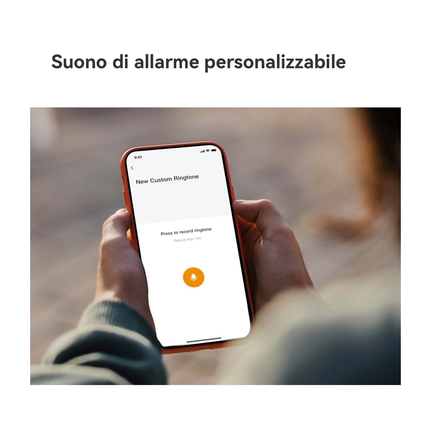 Una persona tiene in mano un telefono che mostra una schermata di registrazione di suoneria personalizzata. Il telefono è arancione, con un'icona del microfono.