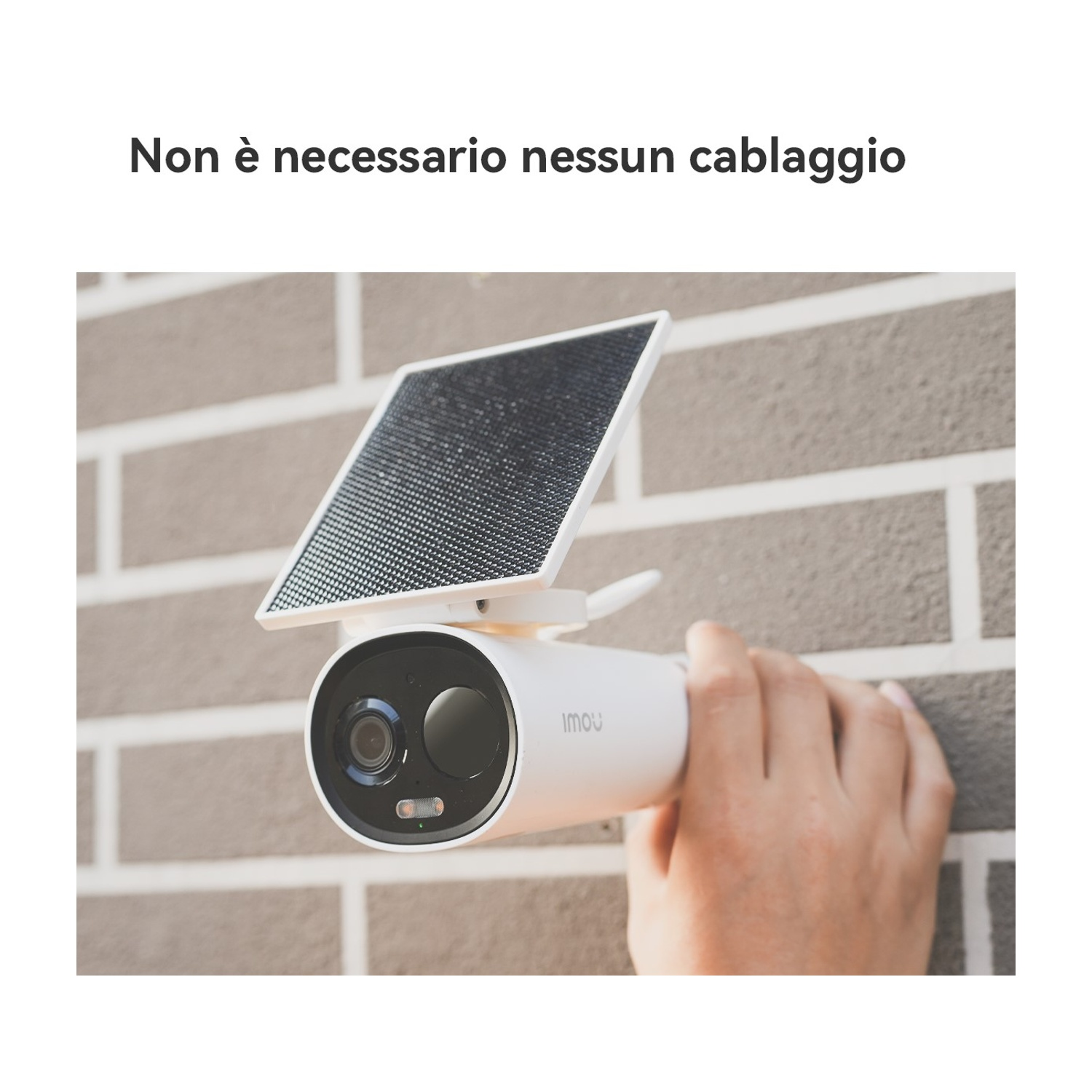 Una telecamera di sicurezza bianca con pannello solare è tenuta in mano. È montata su un muro di mattoni. Il testo sopra dice "Nessun cablaggio necessario".
