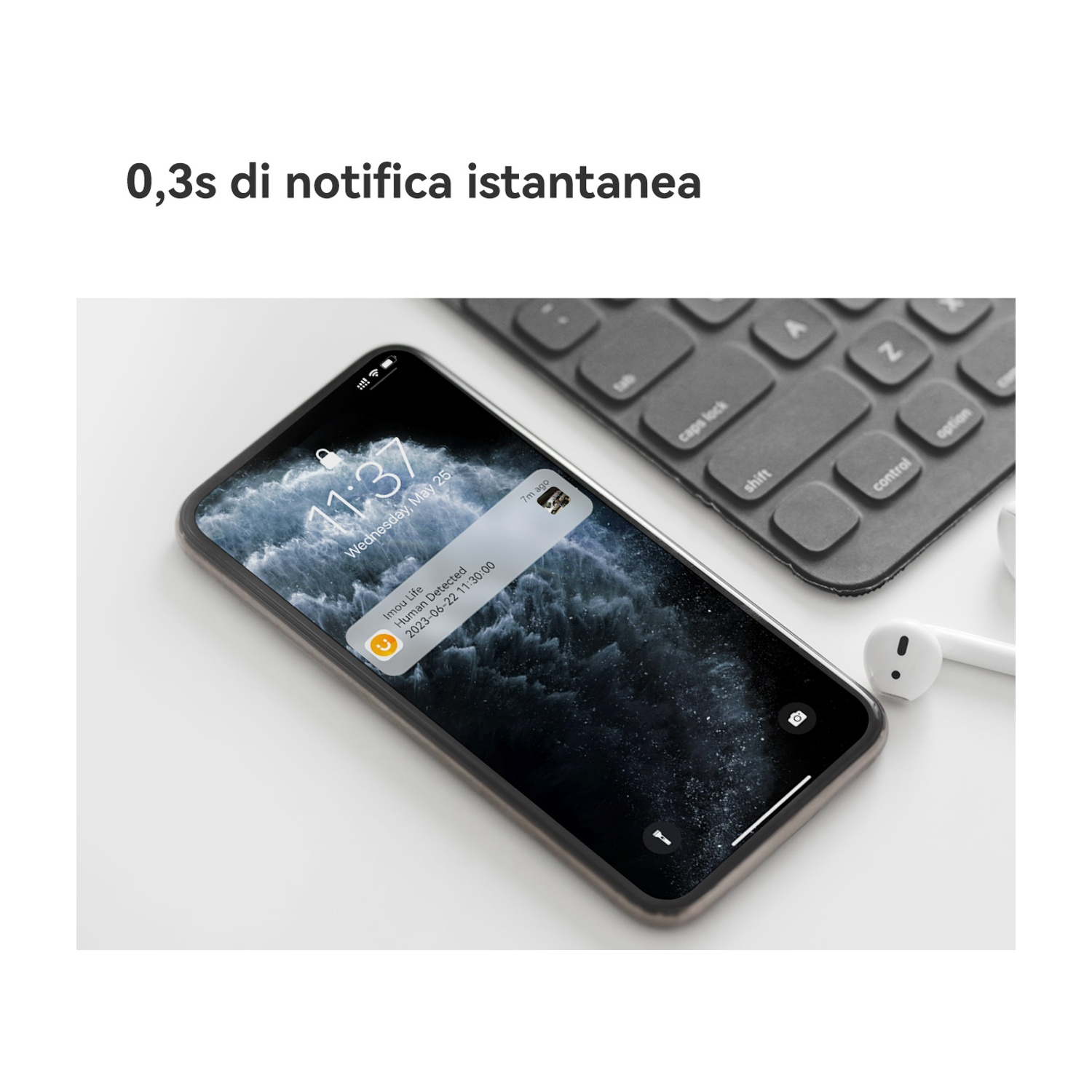 Uno smartphone mostra una notifica di rilevamento umano. Tastiera e auricolari sullo sfondo, su una superficie bianca.