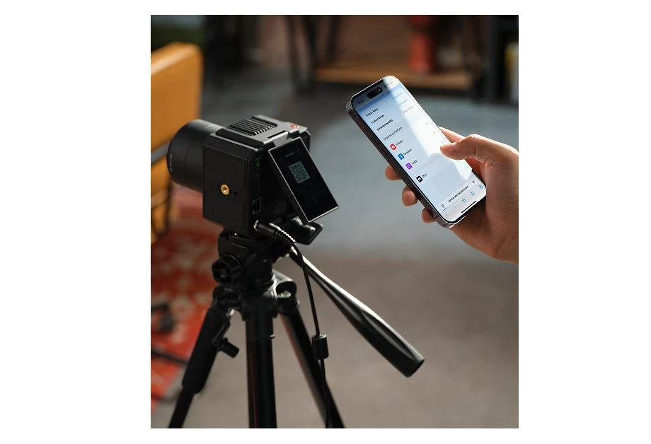 Czarna kamera na statywie obok dłoni trzymającej smartfon. Telefon wyświetla aplikacje mediów społecznościowych.