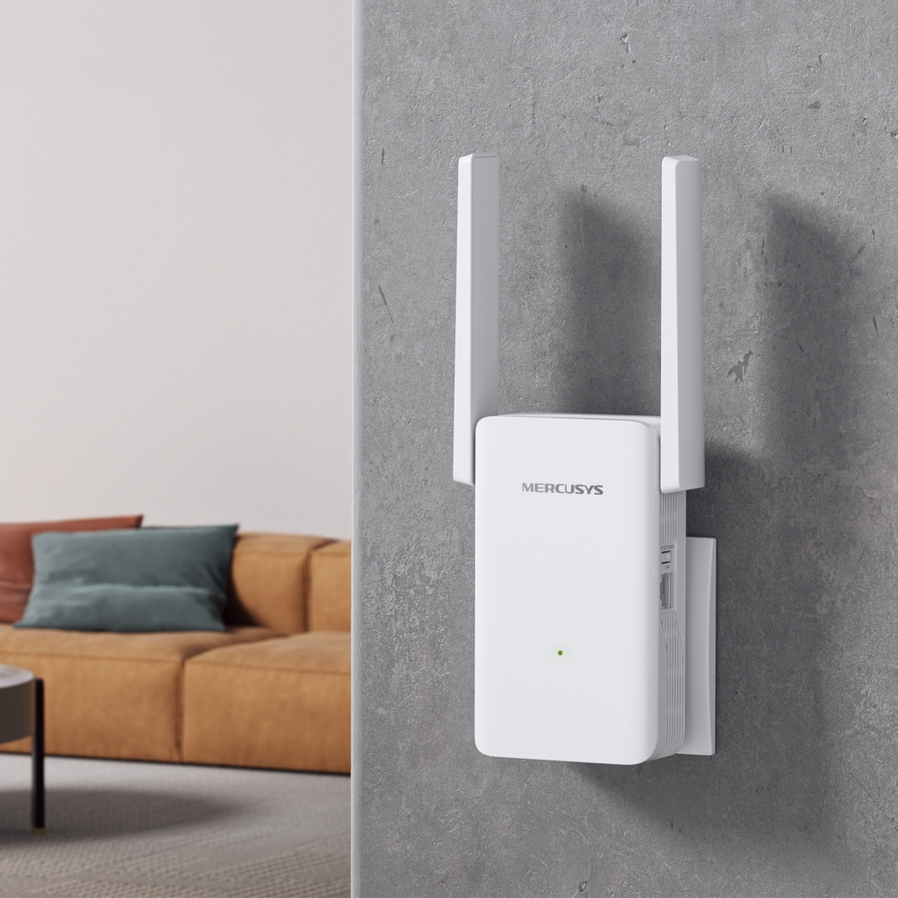 Beyaz bir Mercusys Wi-Fi genişletici gri bir duvara monte edilmiştir. Bulanık arka planda kahverengi bir kanepe ve bir masa var.
