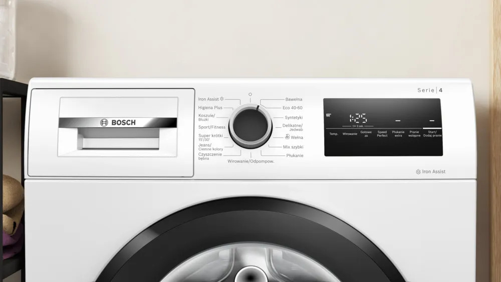 Biała pralka Bosch z panelem sterowania, pokrętłem i wyświetlaczem cyfrowym. Posiada różne opcje cyklu prania.