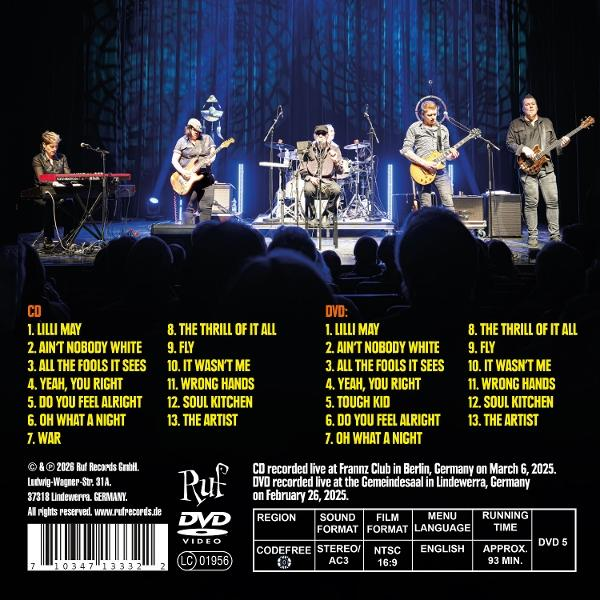 Band spielt auf der Bühne. CD- und DVD-Titellisten auf einem Konzertplakat.