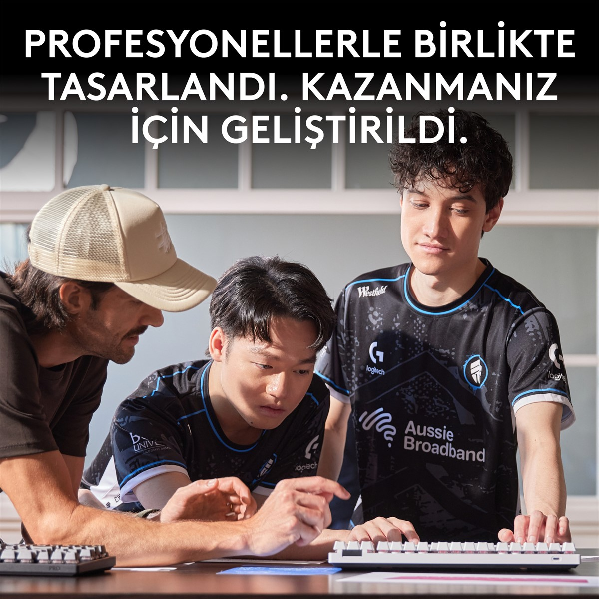 Üç genç adam bir klavyeye bakıyor. Biri şapkalı, diğerleri formalar giymiş. Üstteki metin 'Profesyonellerle tasarlandı' diyor.