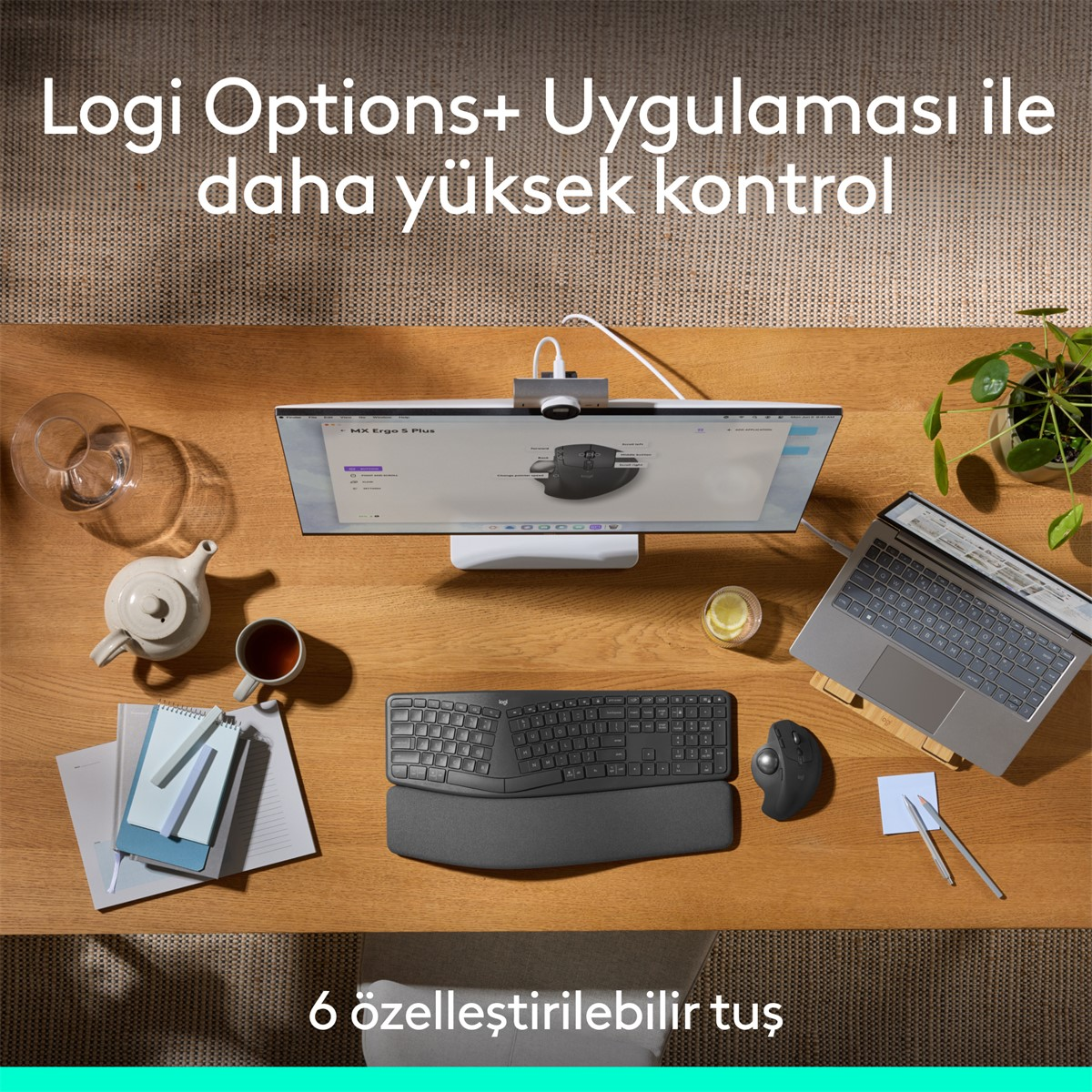 Monitör, klavye, fare, dizüstü bilgisayar, çay takımı ve bitki ile masa düzeni. Monitör bir fare arayüzü görüntüler.