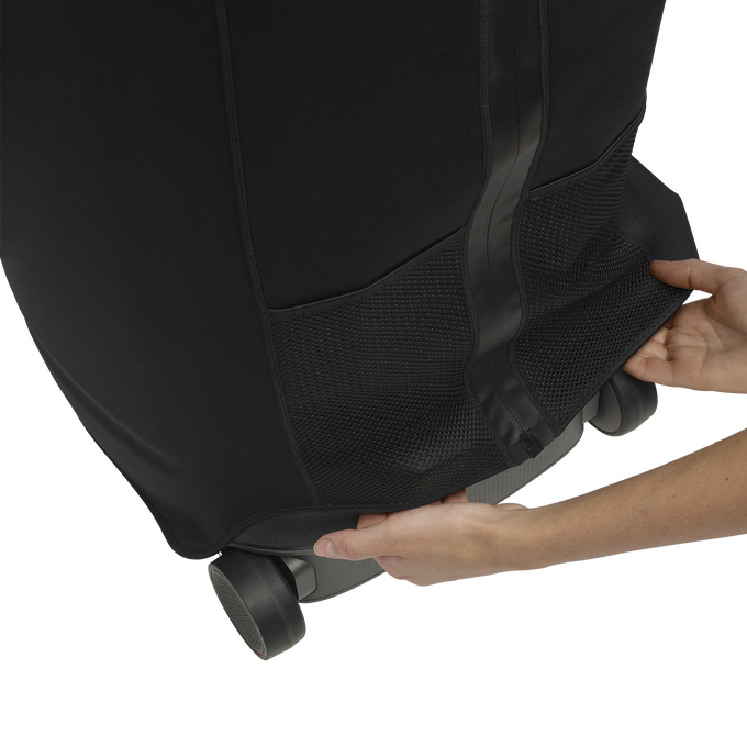 Hände halten eine schwarze Tasche über einem Koffer. Die Tasche hat Netztaschen und bedeckt die Räder.
