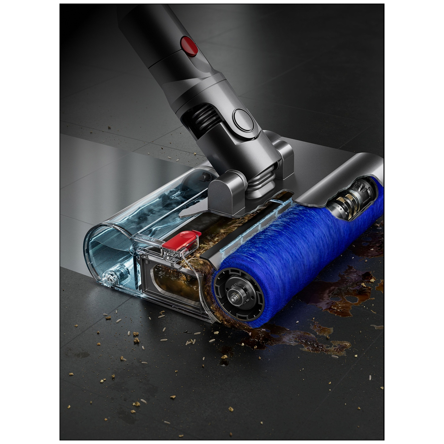Une tête d'aspirateur nettoie un sol sale. La tête a une brosse bleue et un récipient transparent. Le sol est couvert de débris.