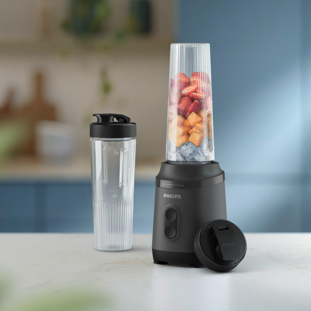 Meyve ve buz dolu bir bardakla bir blender. Yanında siyah kapaklı şeffaf bir bardak var. Blender siyahtır.