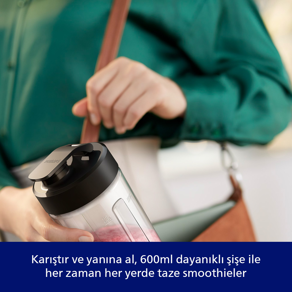 Bir kişi siyah kapaklı bir smoothie yapma makinesi tutuyor. Kişi yeşil bir gömlek giyiyor ve kahverengi bir çanta taşıyor.