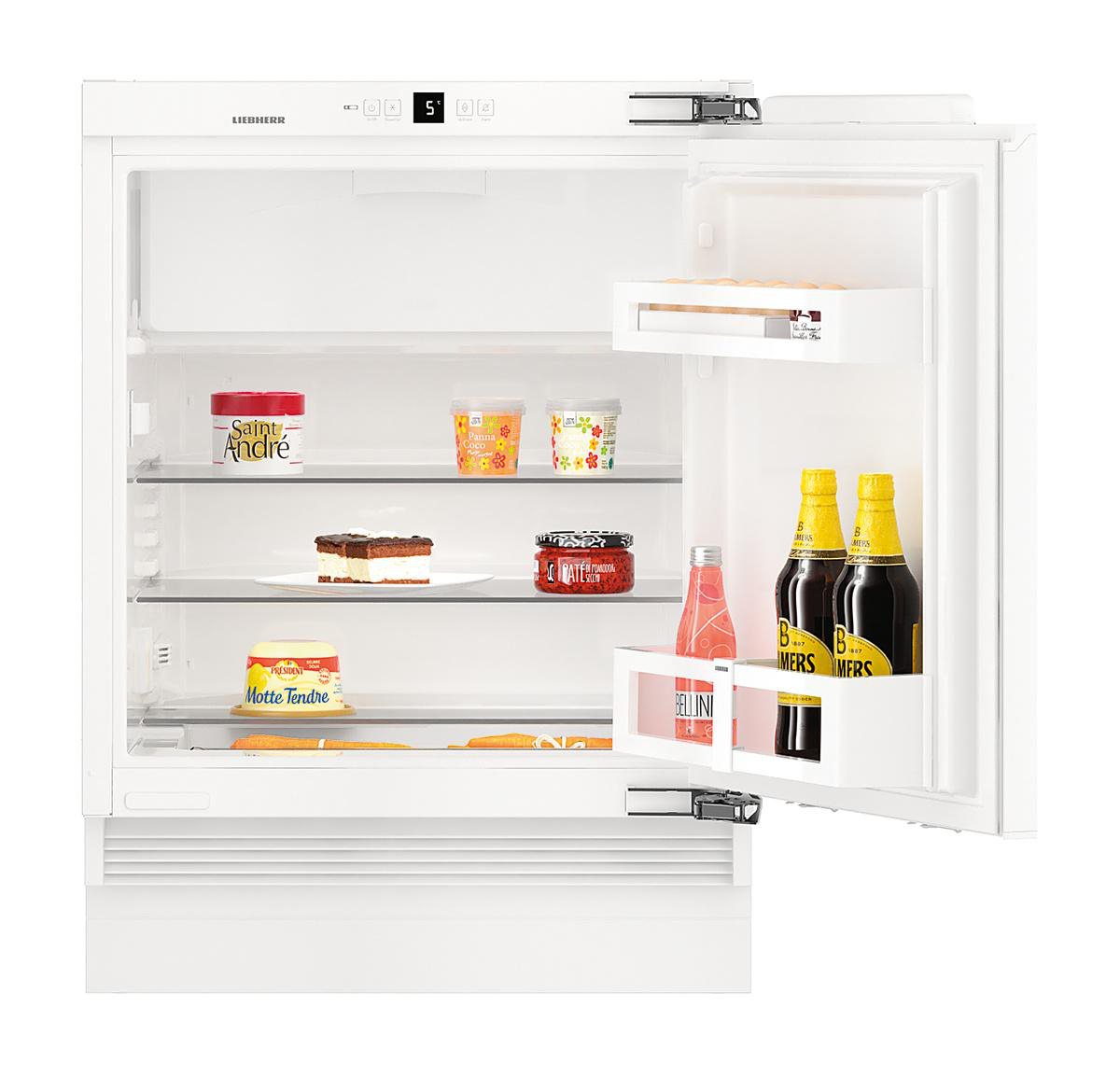 Offener weißer Kühlschrank mit verschiedenen Lebensmitteln: Käse, Kuchen, Gläser, Flaschen. Die Tür ist angelehnt und zeigt das Innere.