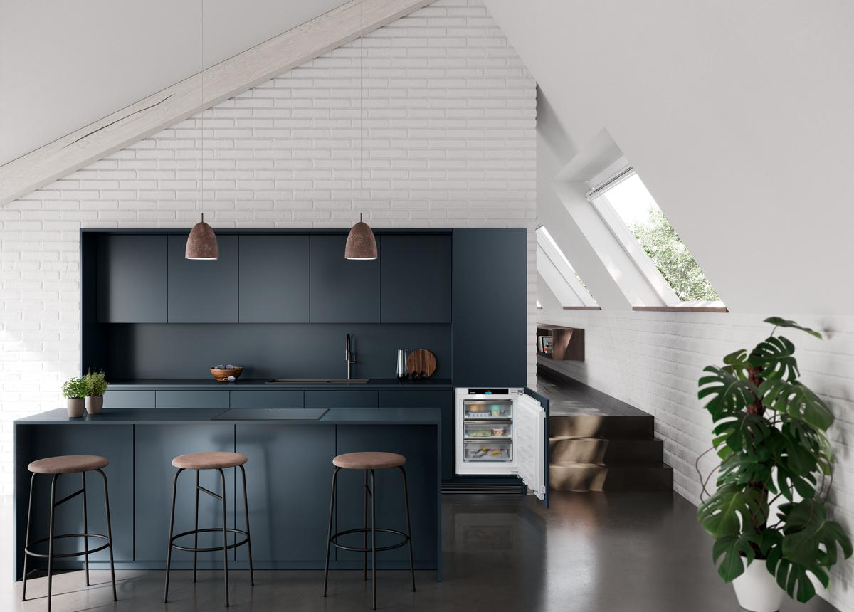 Eine moderne Küche mit blauen Schränken, Barhockern und einem offenen Kühlschrank. Eine große Zimmerpflanze und Oberlichter im Hintergrund.
