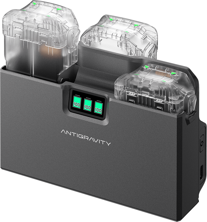 Une station de charge Antigravity gris foncé avec trois baies de charge. Chaque baie contient une batterie avec un couvercle transparent. Trois écrans affichent 100%.